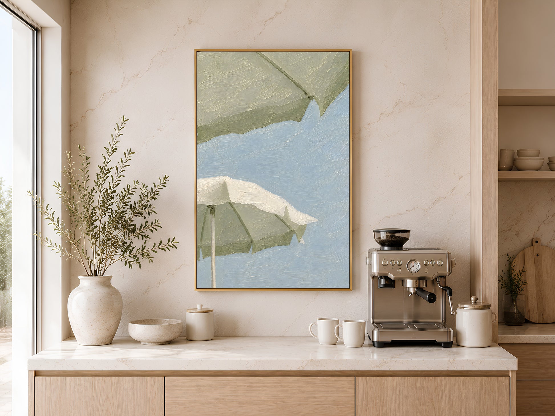 Sage green beach umbrella wall art in a wood frame displayed above a coffee station in a warm minimalist kitchen with cream cabinetry and dried botanicals
