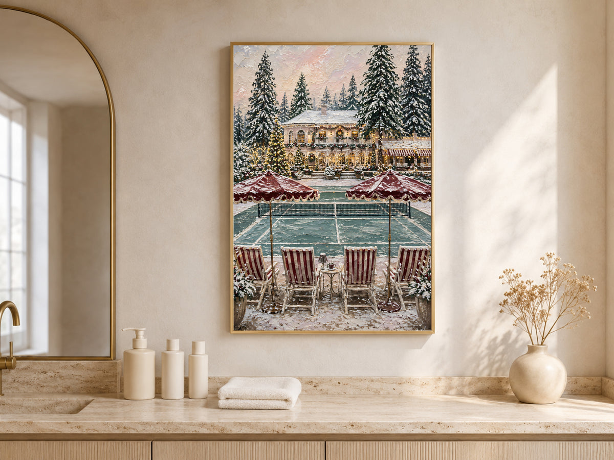 Framed winter estate Christmas painting displayed on a console table beneath an arched mirror above a bathroom counter