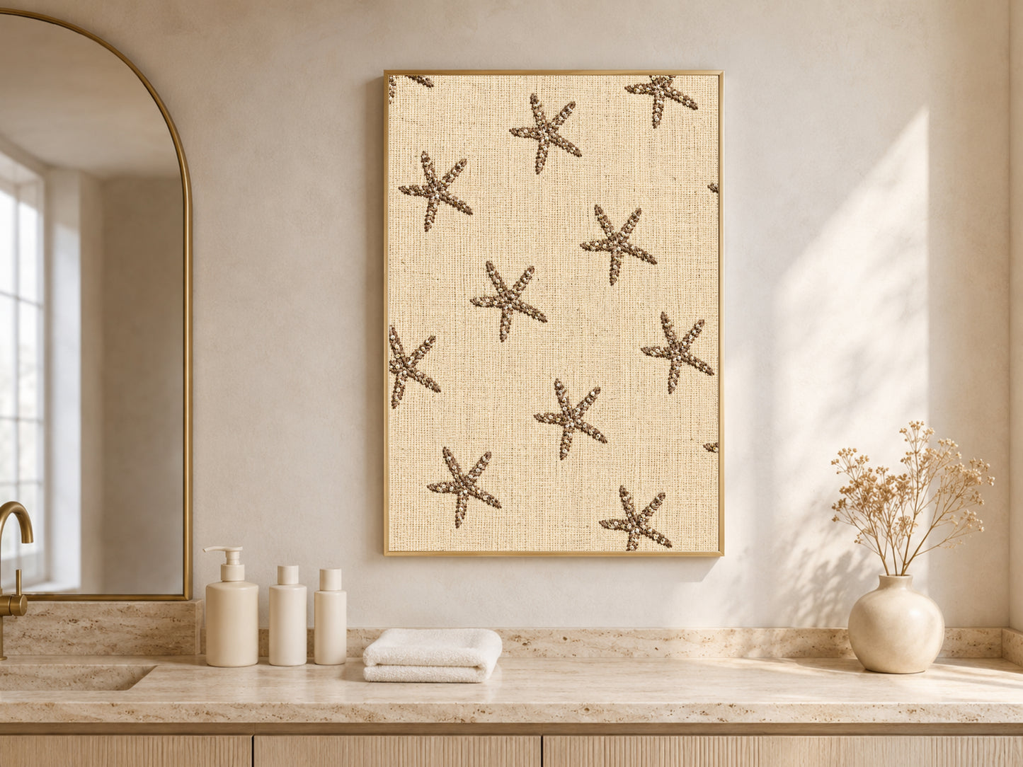 Embroidered starfish wall art framed above a bathroom counter with candles and towels