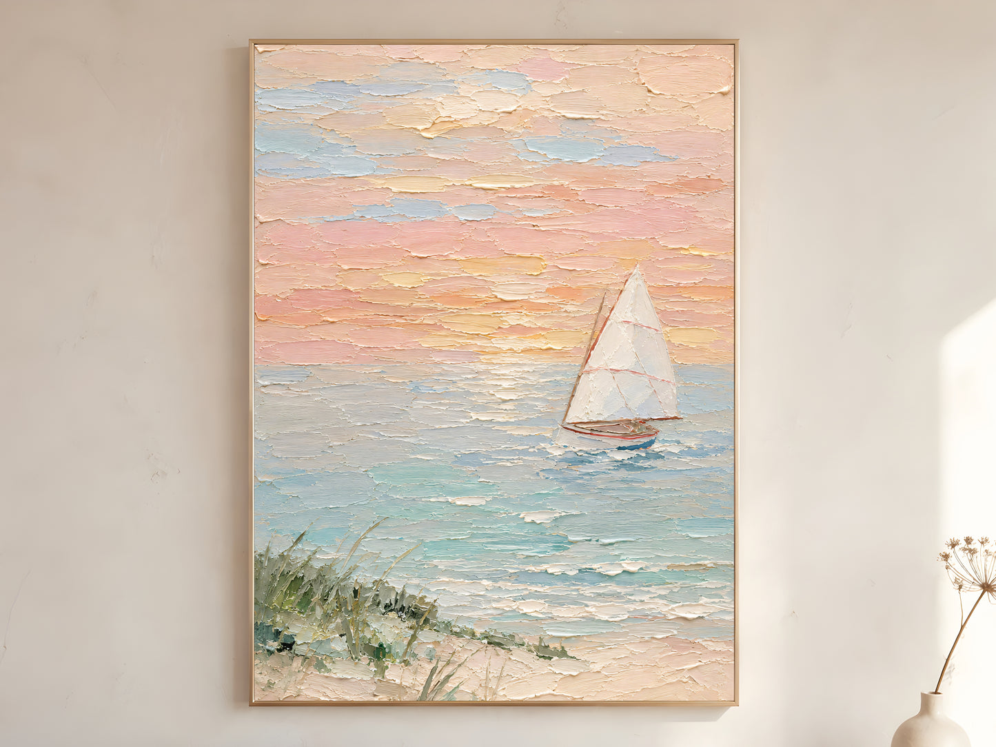 Large framed pastel sailboat sunset impasto wall art print showing white sail on teal sea with peach blush and butter yellow sky and sea grass foreground on warm white wall with dried flower stem
