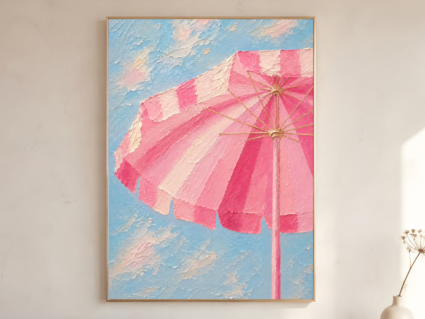 Pink striped beach umbrella impasto wall art print against a blue sky in a gold frame leaning against a warm white wall with dried stems
