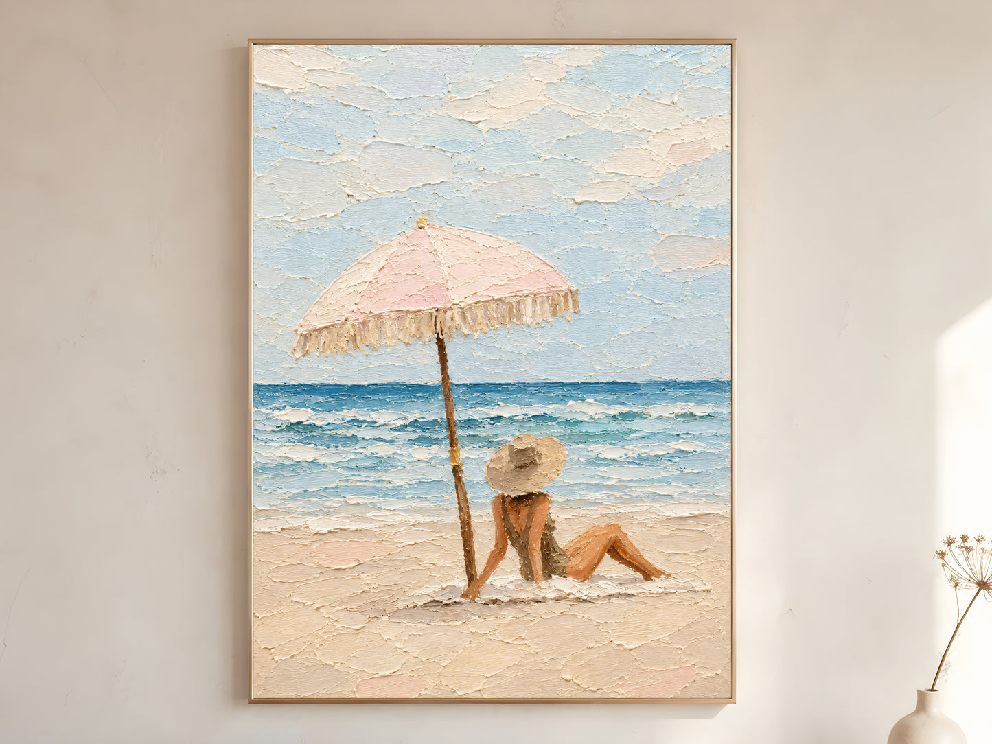 Large framed pastel beach scene impasto wall art print showing woman in sun hat reclining under pink fringed umbrella beside teal ocean on warm white wall
