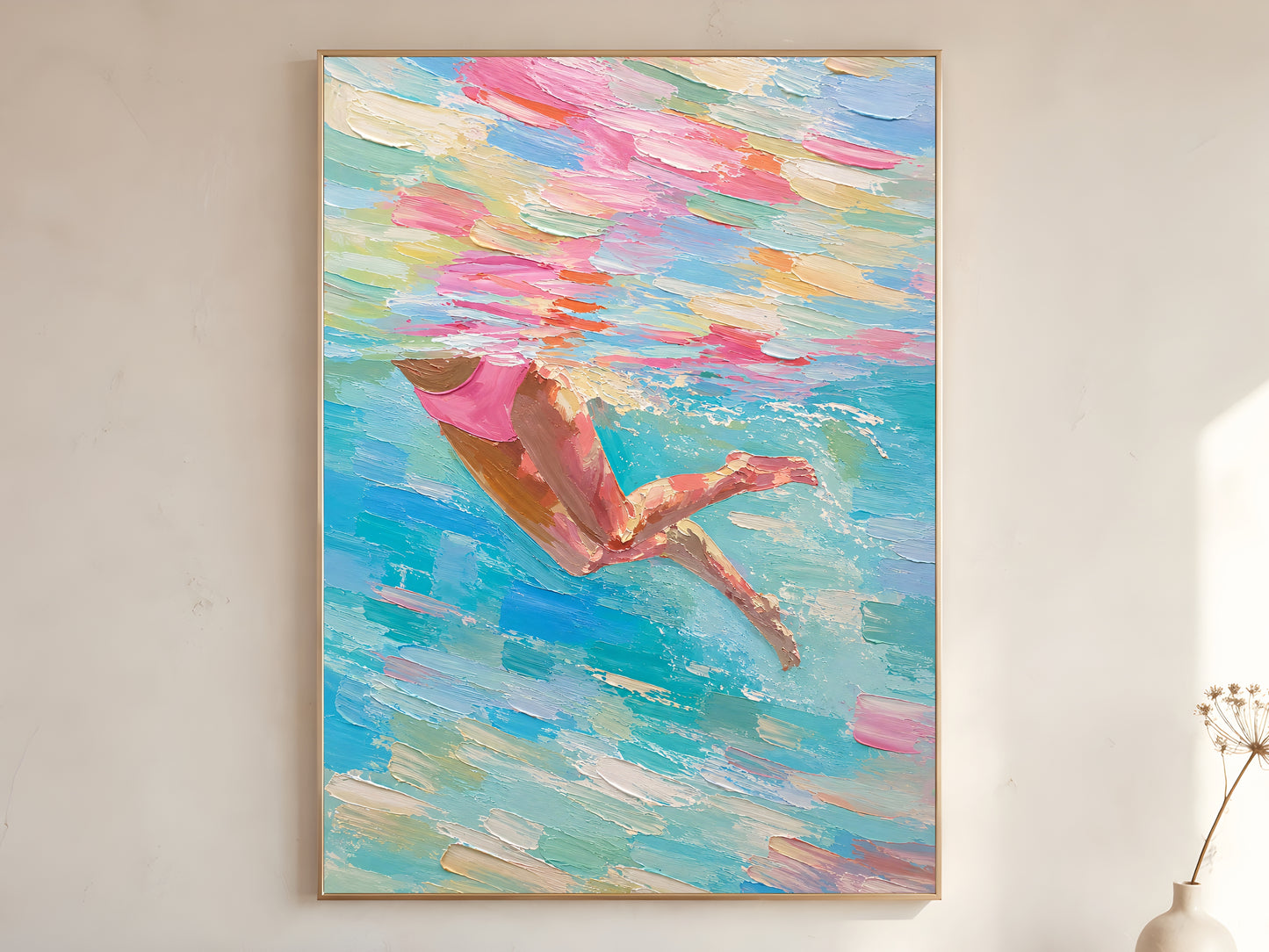 Woman swimmer diving impasto oil painting print in a gold frame leaning against a warm white wall with dried botanicals, showing the full painting with pink swimsuit and swirling teal, blush, coral, and seafoam green water strokes
