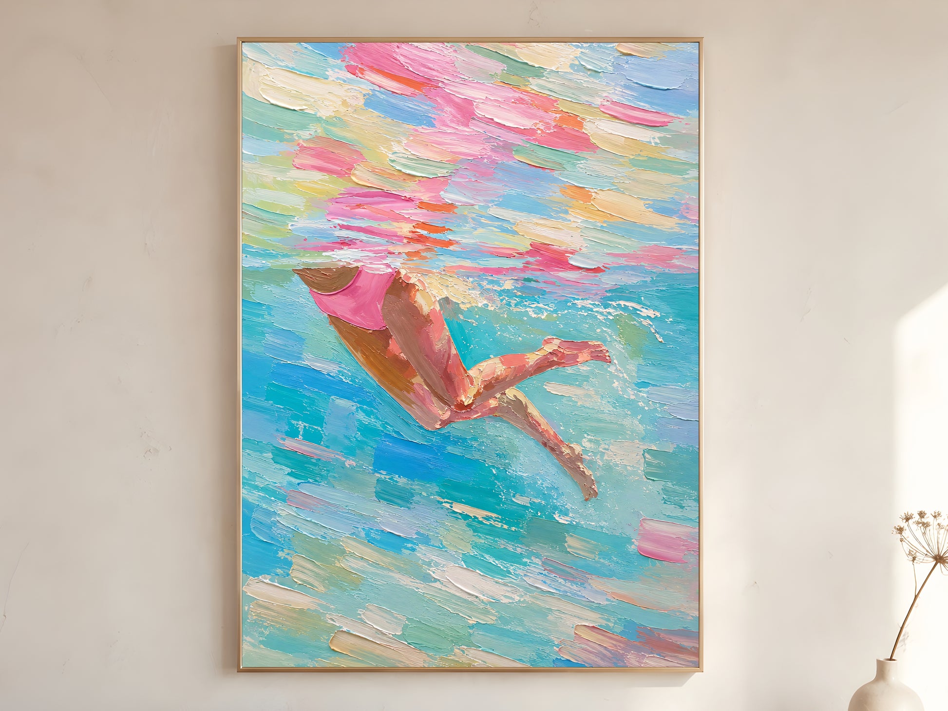 Woman swimmer diving impasto oil painting print in a gold frame leaning against a warm white wall with dried botanicals, showing the full painting with pink swimsuit and swirling teal, blush, coral, and seafoam green water strokes
