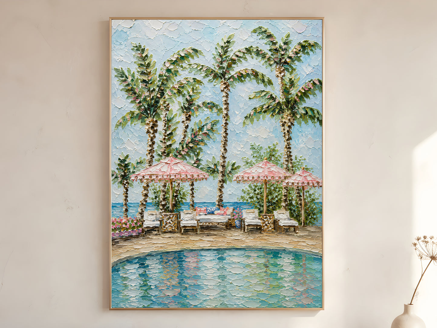 Tropical resort pool with pink fringed parasols, white loungers, and tall palm trees impasto oil painting print in a thin natural wood frame, leaning against a warm white wall with a dried wildflower stem
