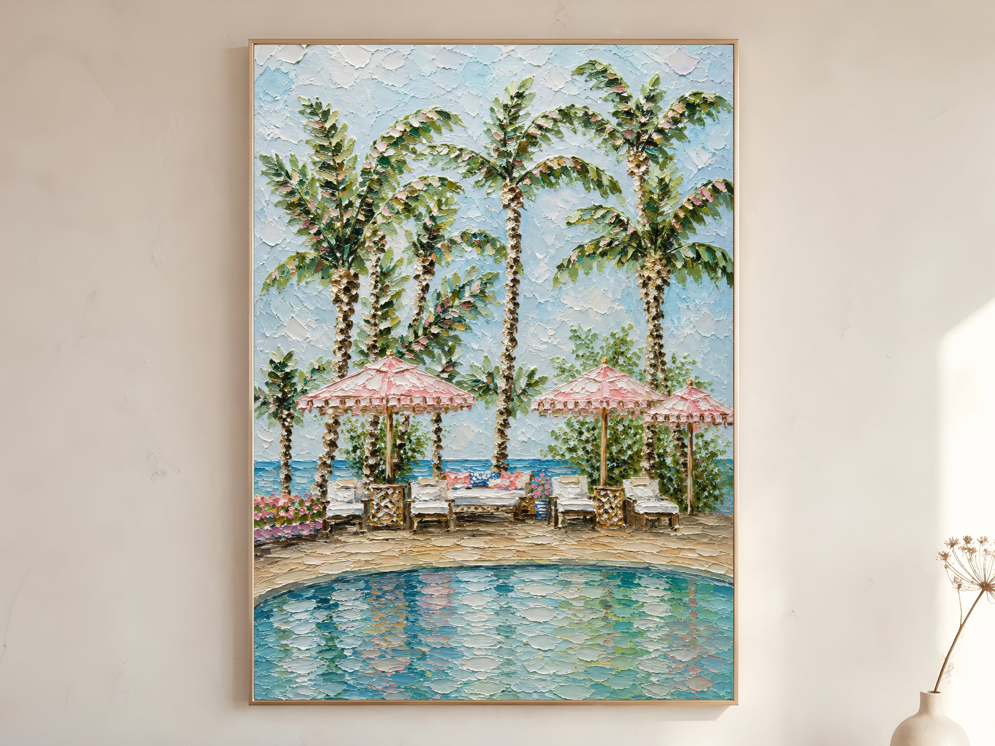 Tropical resort pool with pink fringed parasols, white loungers, and tall palm trees impasto oil painting print in a thin natural wood frame, leaning against a warm white wall with a dried wildflower stem
