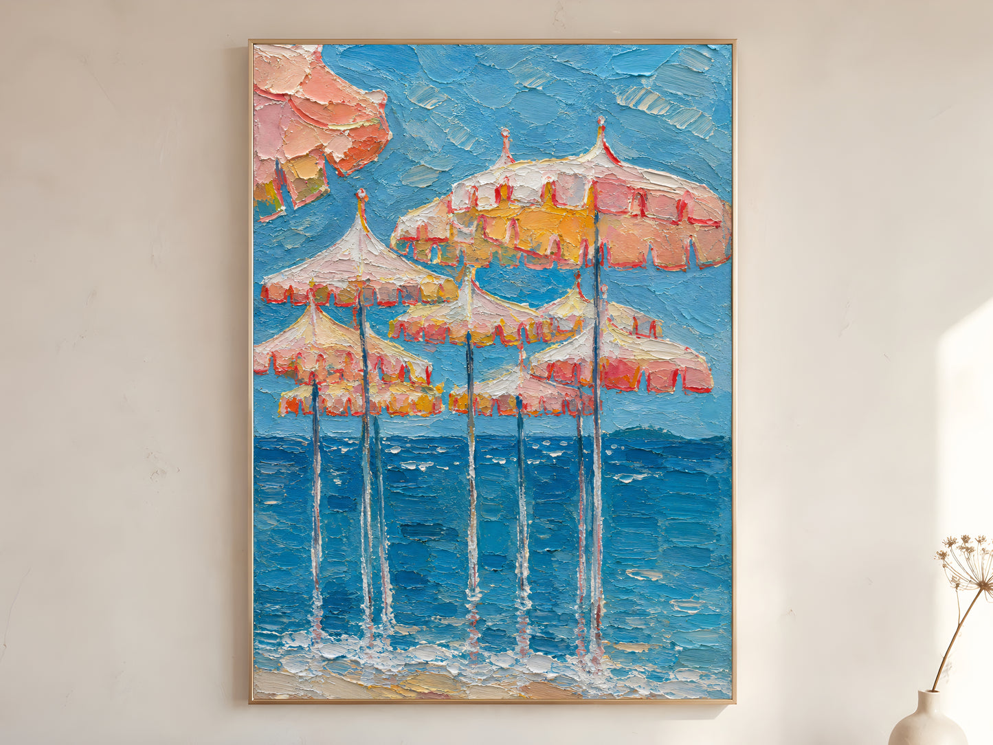 Pink and peach beach umbrella impasto oil painting print in a thin natural wood frame, leaning against a warm white wall with a dried wildflower stem
