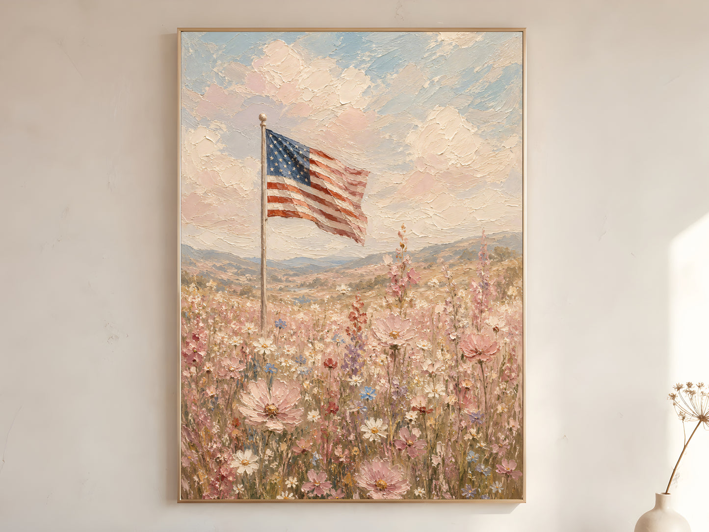 American flag wildflower field impasto oil painting print in a gold frame leaning against a warm white wall with dried botanicals, showing the full painting with pink cosmos, white daisies, rolling hills, and chalky pastel sky

