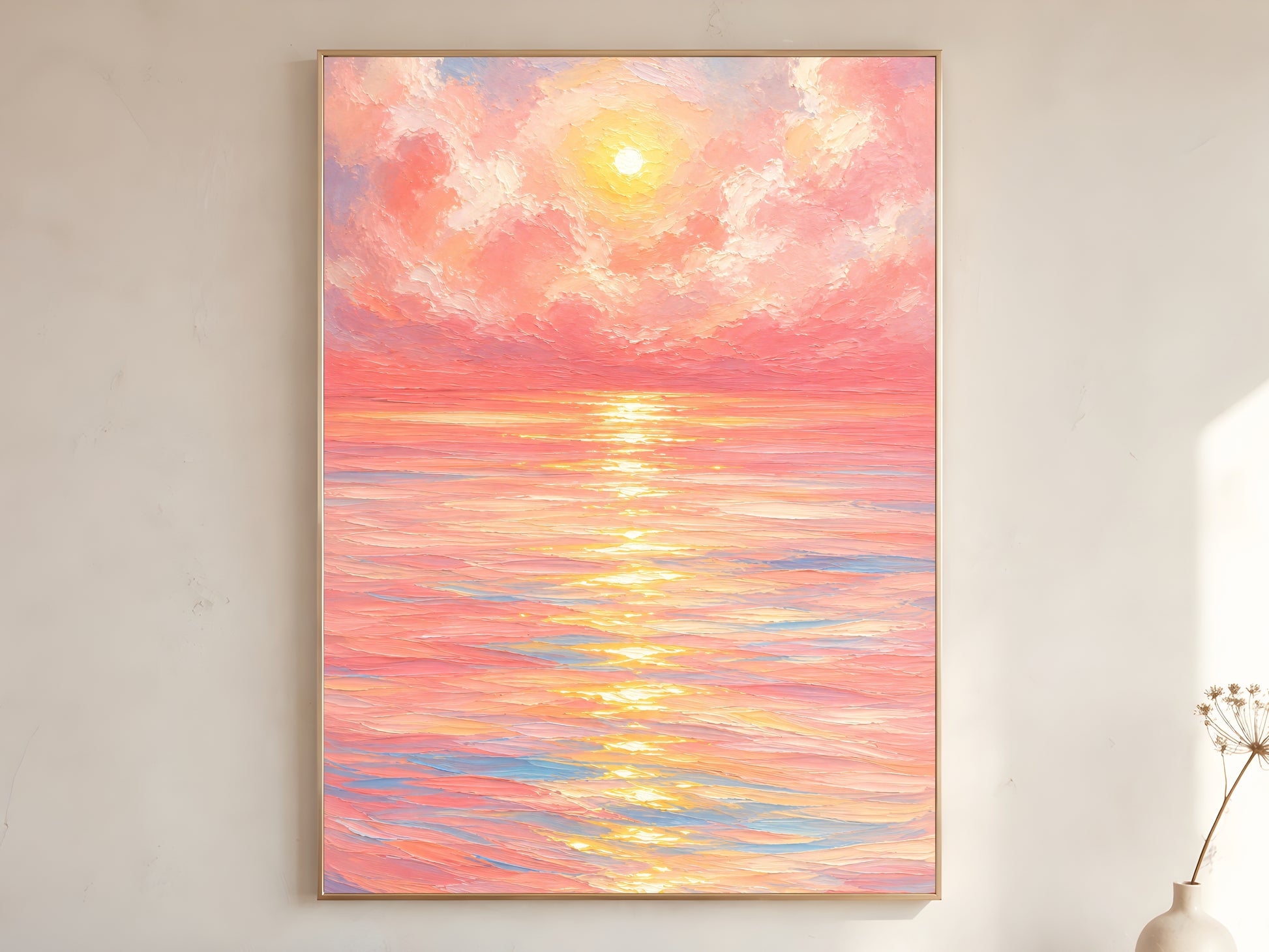 Large framed impasto pink sunset ocean wall art in gold frame leaning against white wall with dried botanicals in bright minimal room
