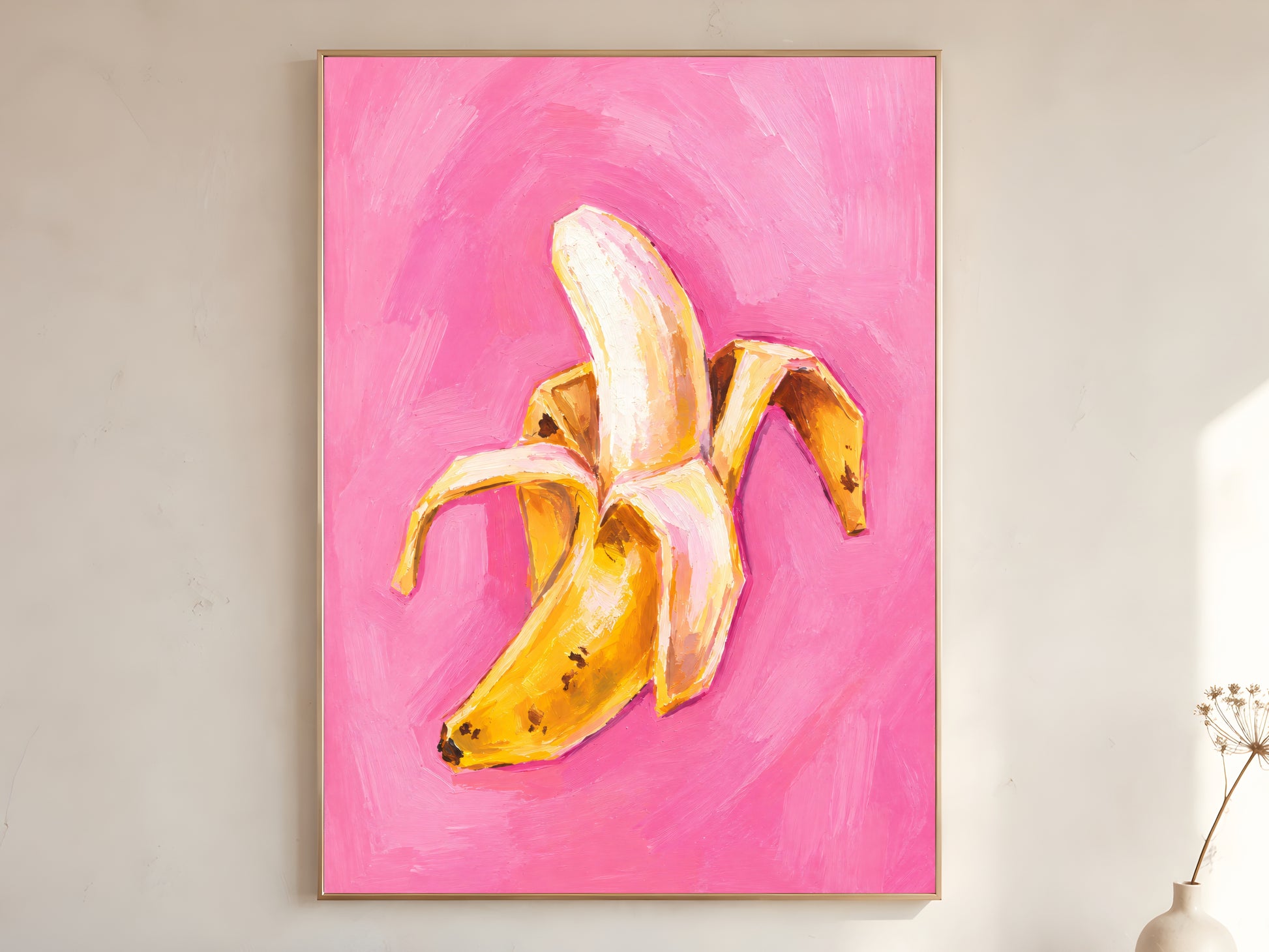 Large framed impasto peeled banana wall art in gold frame leaning against white wall with dried botanicals in bright minimal room
