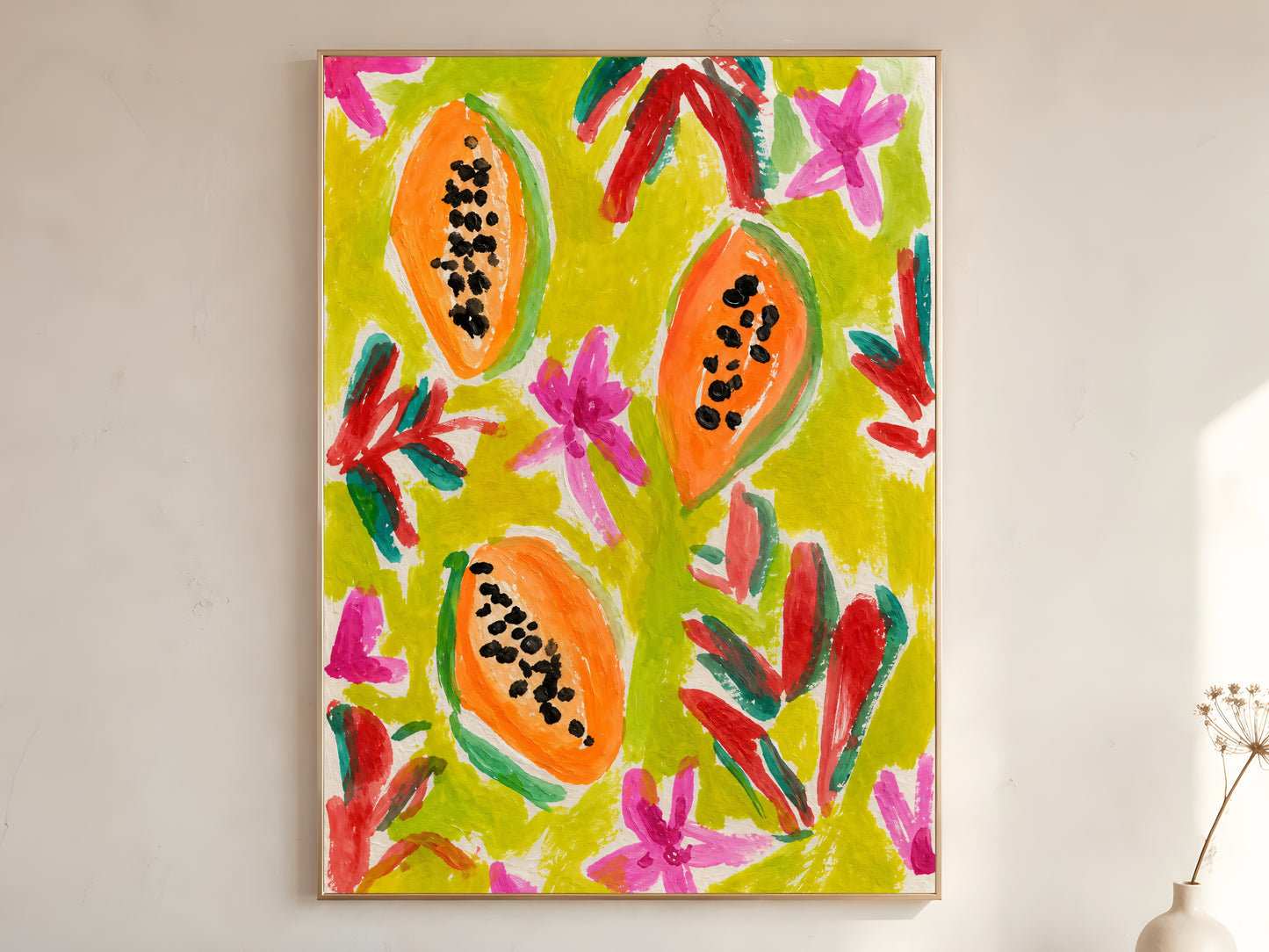 Colorful papaya wall art print in a gold frame leaning against a warm white wall with dried botanicals, showing the full bold illustration with orange papayas, chartreuse background, hot pink blooms, and expressive red and teal brushstrokes
