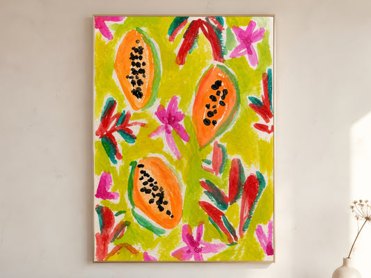 Colorful papaya wall art print in a gold frame leaning against a warm white wall with dried botanicals, showing the full bold illustration with orange papayas, chartreuse background, hot pink blooms, and expressive red and teal brushstrokes
