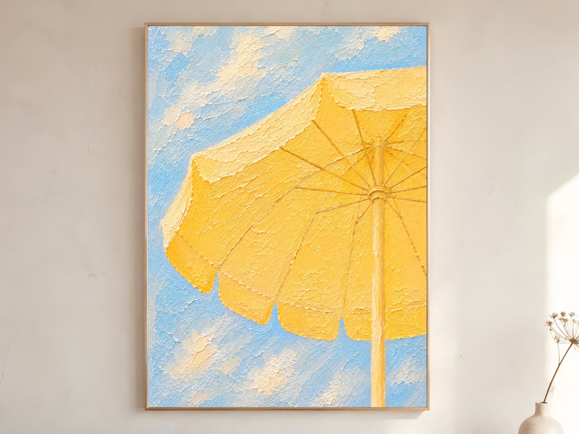 Yellow beach umbrella impasto wall art print against a blue sky in a gold frame leaning against a warm white wall with dried stems
