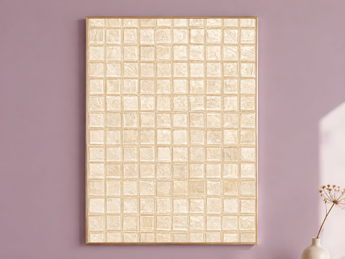 Warm beige impasto mosaic tile wall art in a thin gold frame leaning against a dusty mauve wall with a dried allium stem in a cream vase beside it

