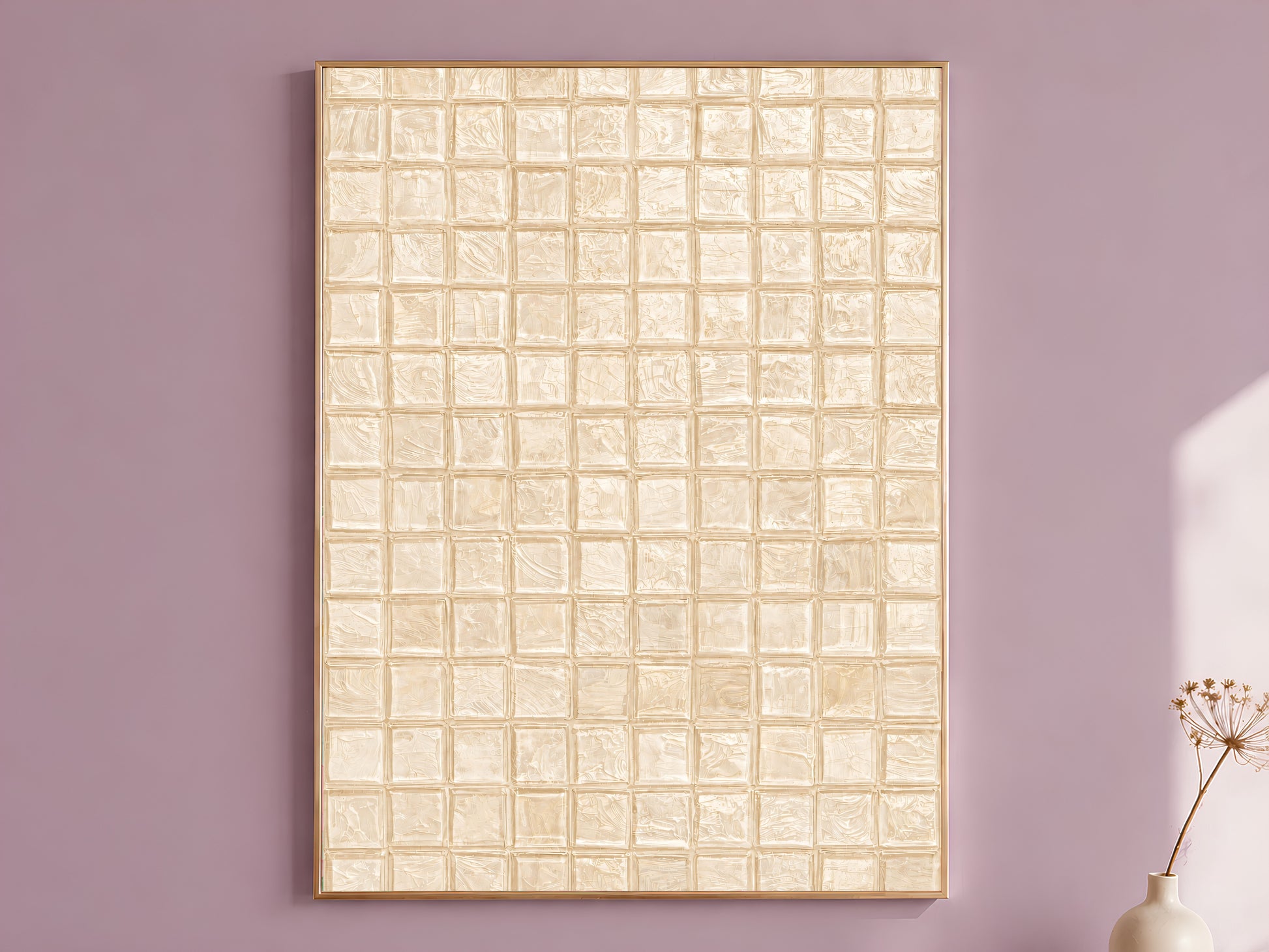 Warm beige impasto mosaic tile wall art in a thin gold frame leaning against a dusty mauve wall with a dried allium stem in a cream vase beside it

