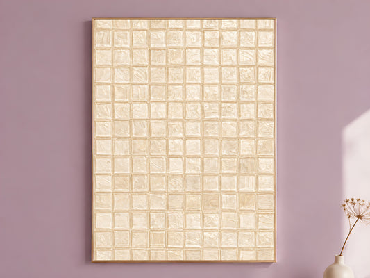 Warm beige impasto mosaic tile wall art in a thin gold frame leaning against a dusty mauve wall with a dried allium stem in a cream vase beside it

