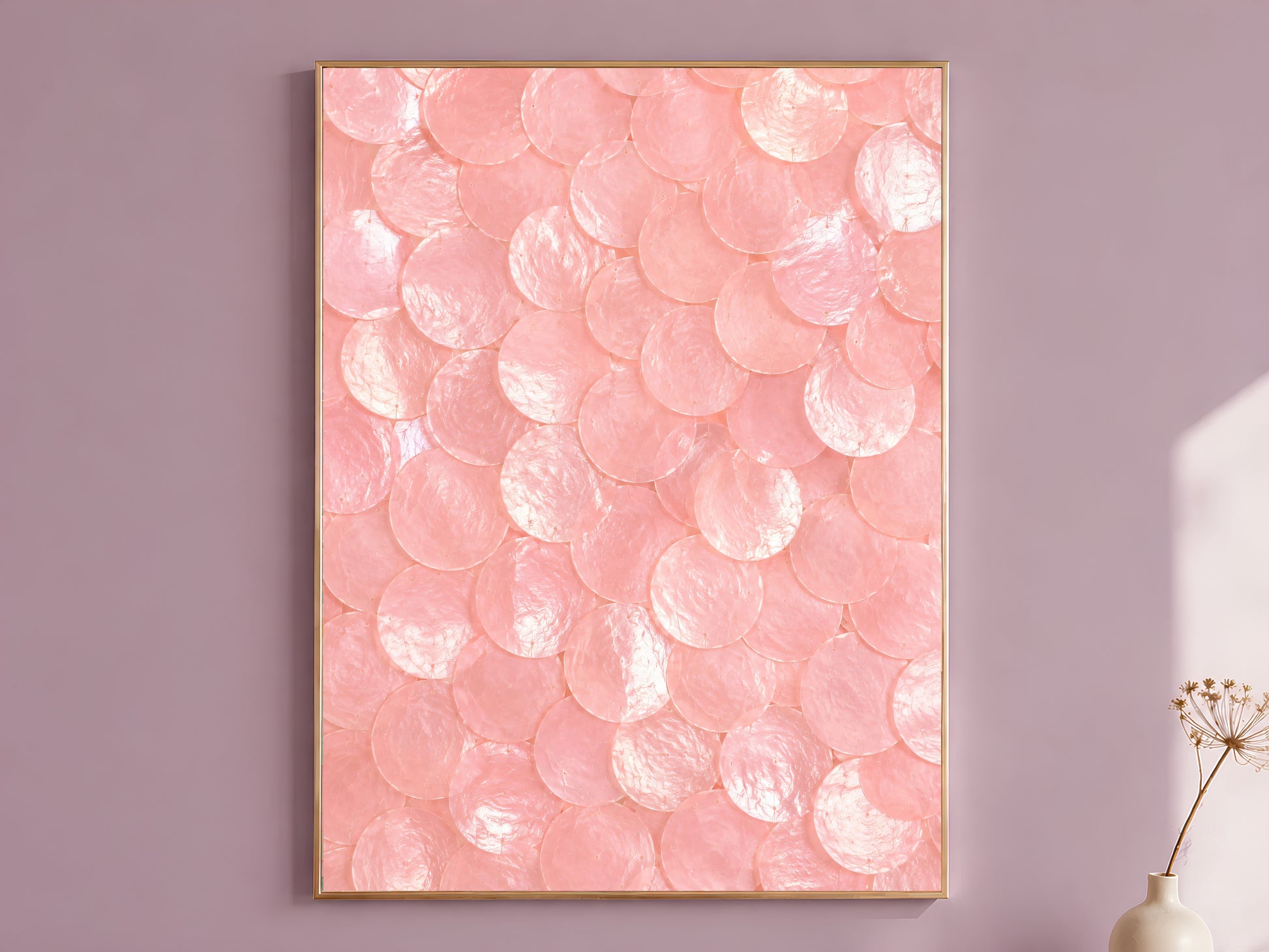 Pink capiz shell dot print in a thin gold frame, hung on a mauve wall with a vase of dried flowers.
