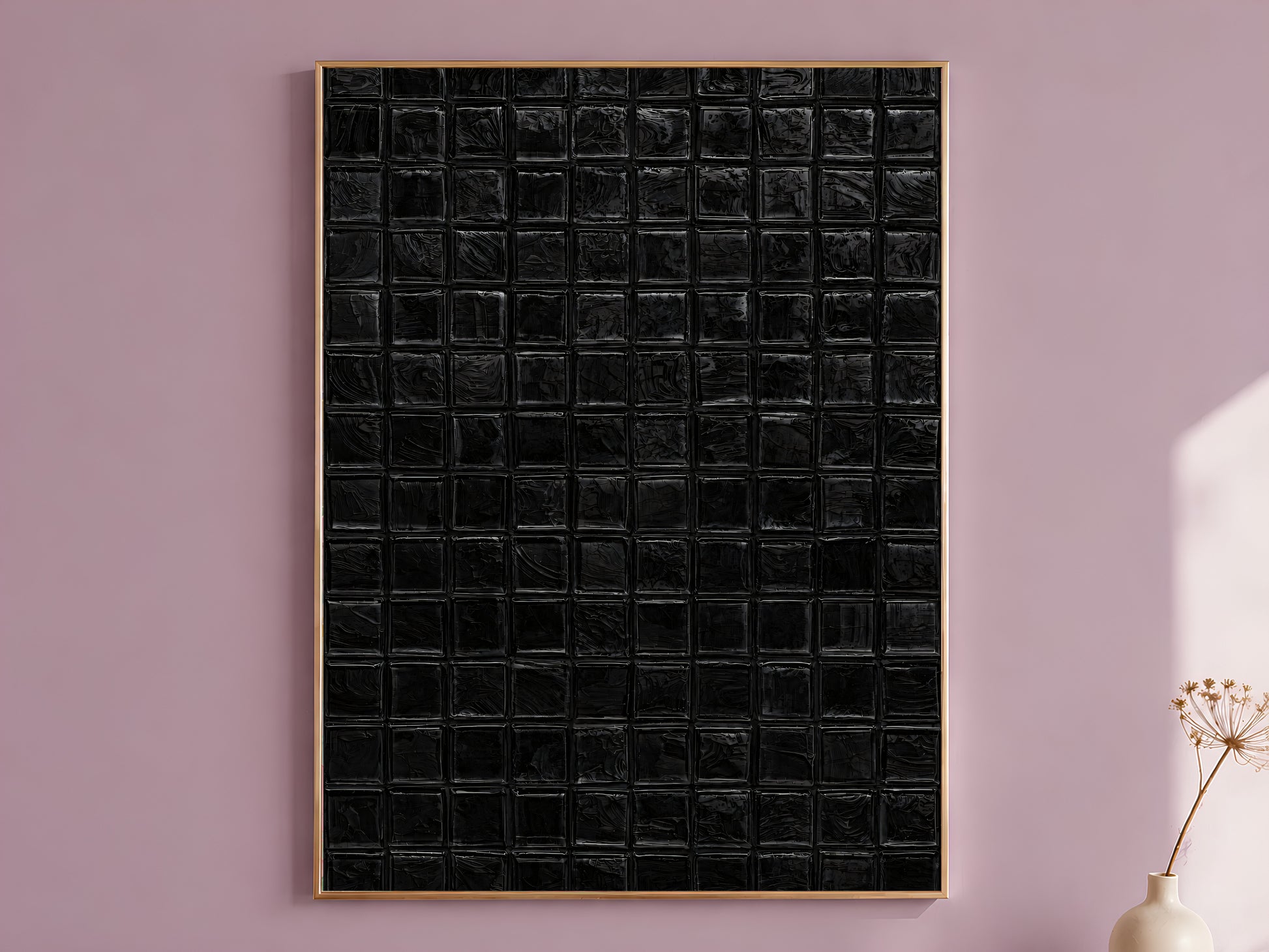 Black impasto mosaic tile wall art in a thin gold frame leaning against a dusty mauve wall with a dried allium stem in a cream vase beside it

