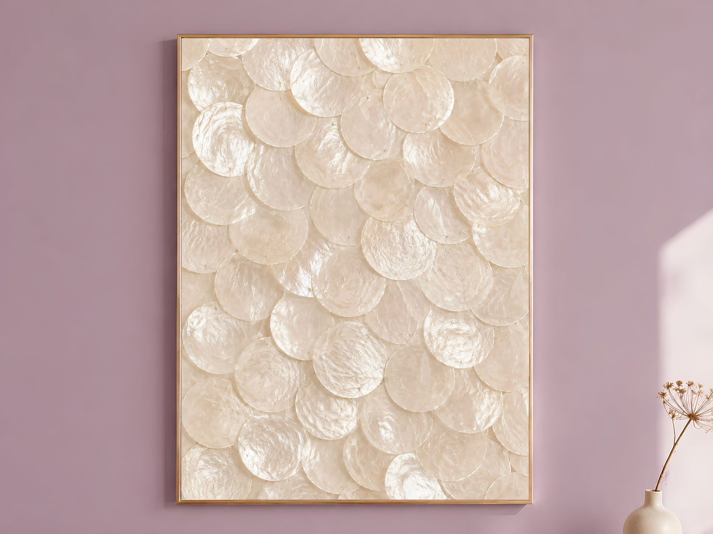 Capiz shell wall art in white and oyster pearl, framed in thin gold, hung on a dusty mauve wall beside a vase of dried flowers

