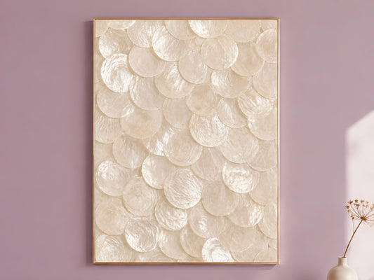 Capiz shell wall art in white and oyster pearl, framed in thin gold, hung on a dusty mauve wall beside a vase of dried flowers
