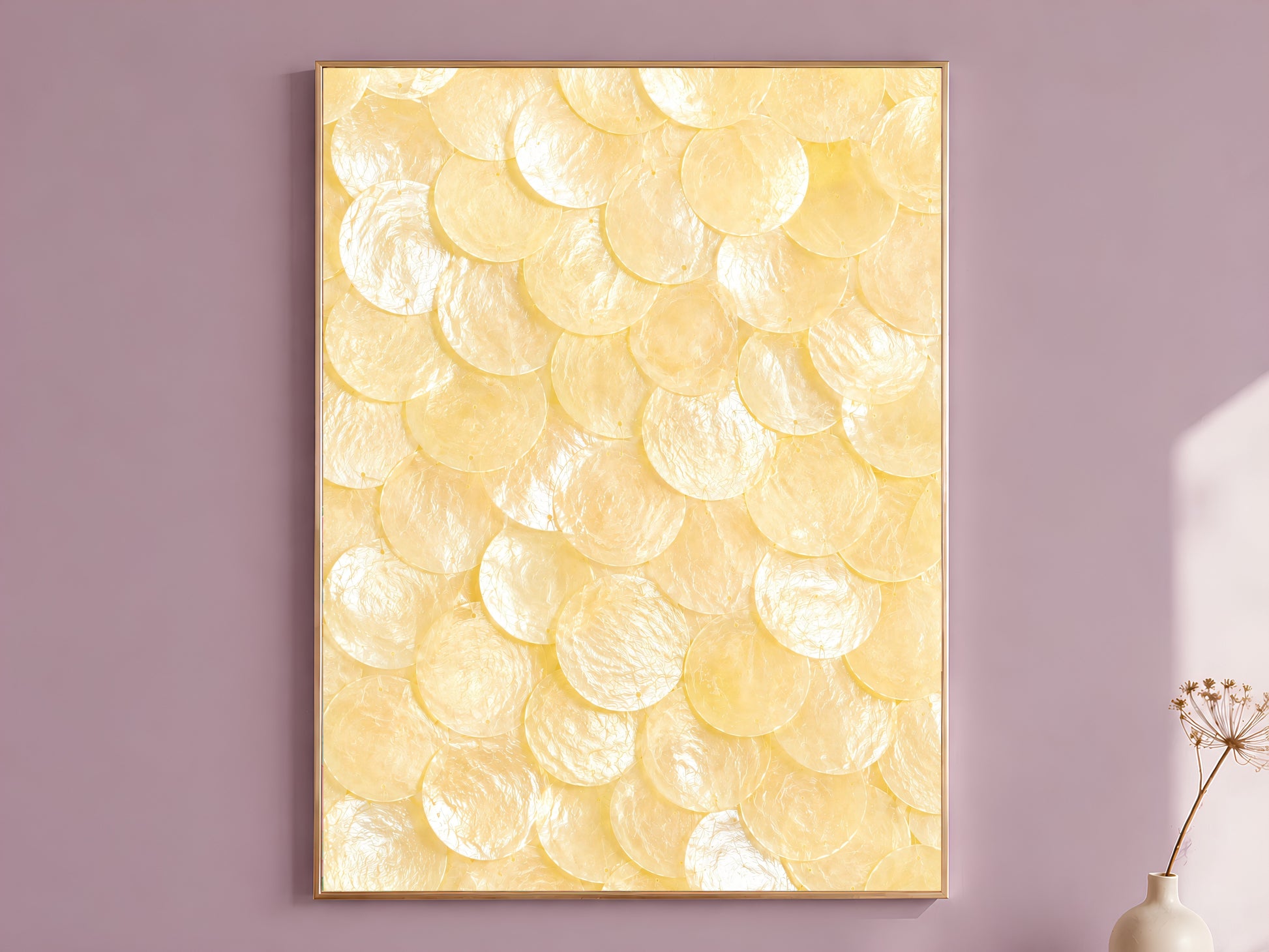 Capiz shell wall art in butter yellow and ivory, framed in thin gold, hung on a dusty mauve wall beside a vase of dried flowers
