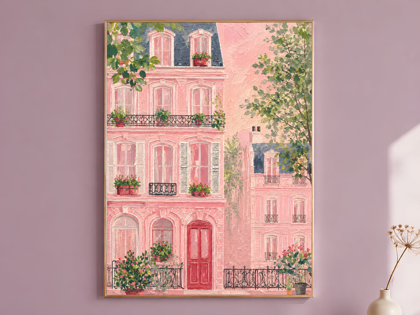 Impasto oil painting pink Parisian building wall art in a thin gold frame leaning against a dusty mauve wall with a dried allium stem in a cream vase beside it
