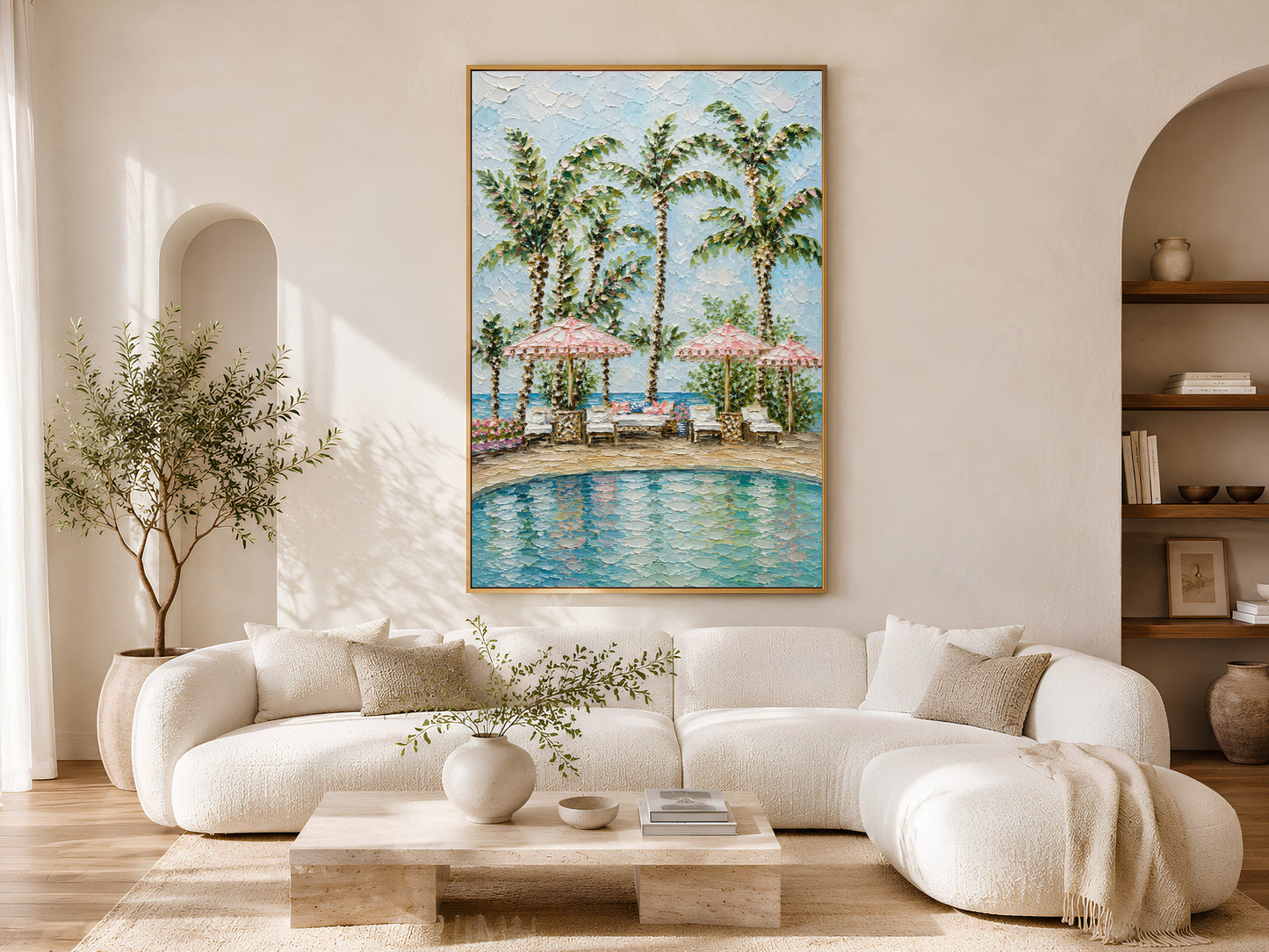 Gold-framed resort pool pink parasol wall art above a low cream sofa in a bright minimalist living room with a round coffee table, olive tree, and warm natural light
