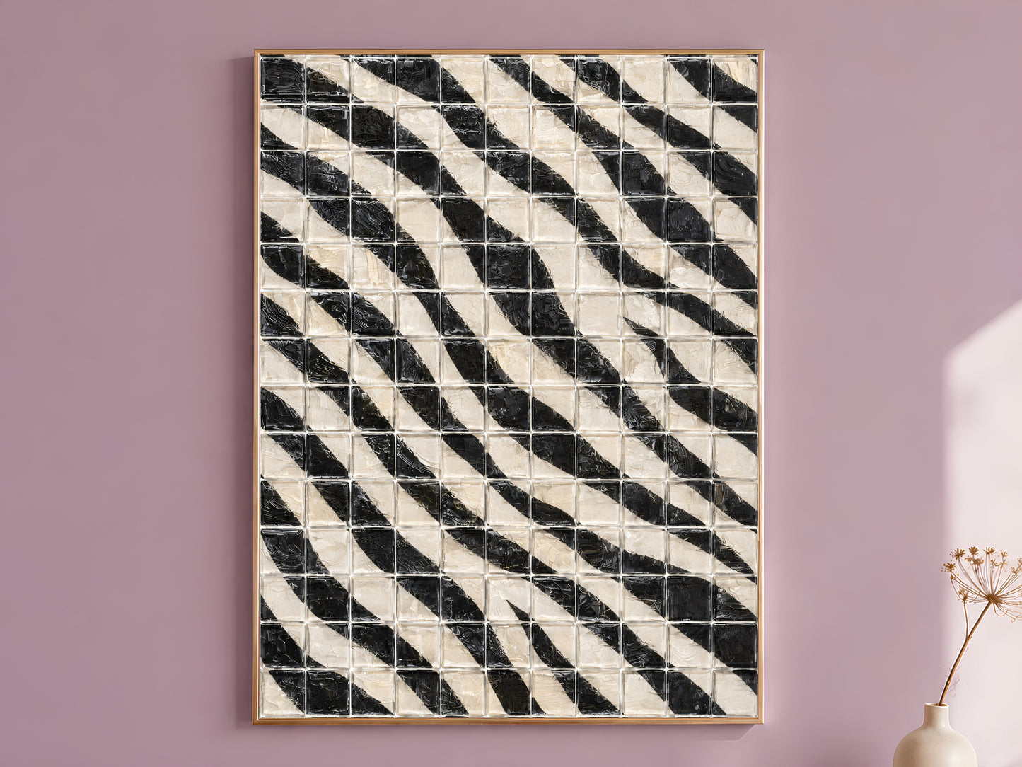 Black and white diagonal stripe mosaic tile wall art in a thin gold frame leaning against a dusty mauve wall with a dried allium stem in a cream vase beside it
