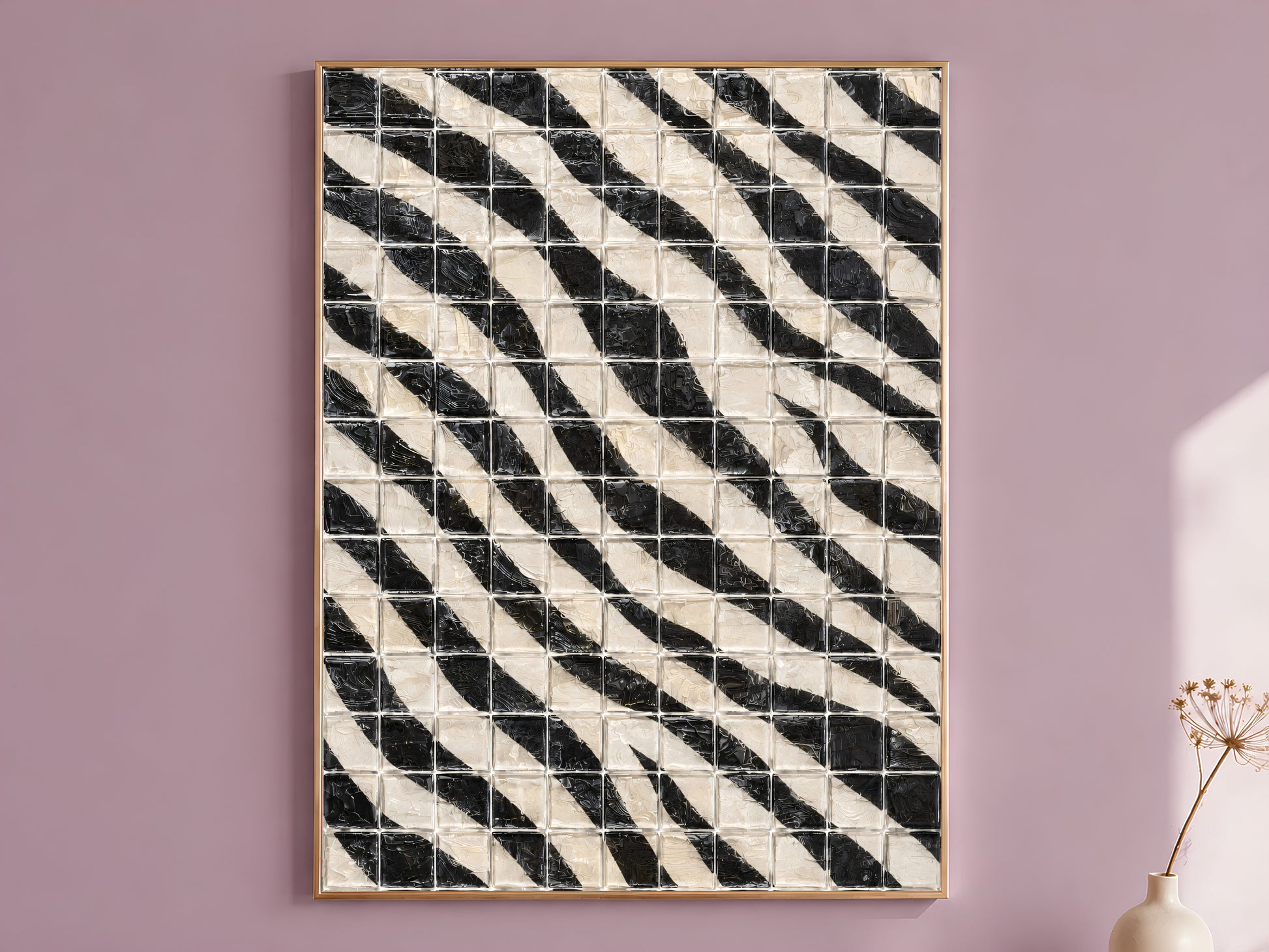 Black and white diagonal stripe mosaic tile wall art in a thin gold frame leaning against a dusty mauve wall with a dried allium stem in a cream vase beside it
