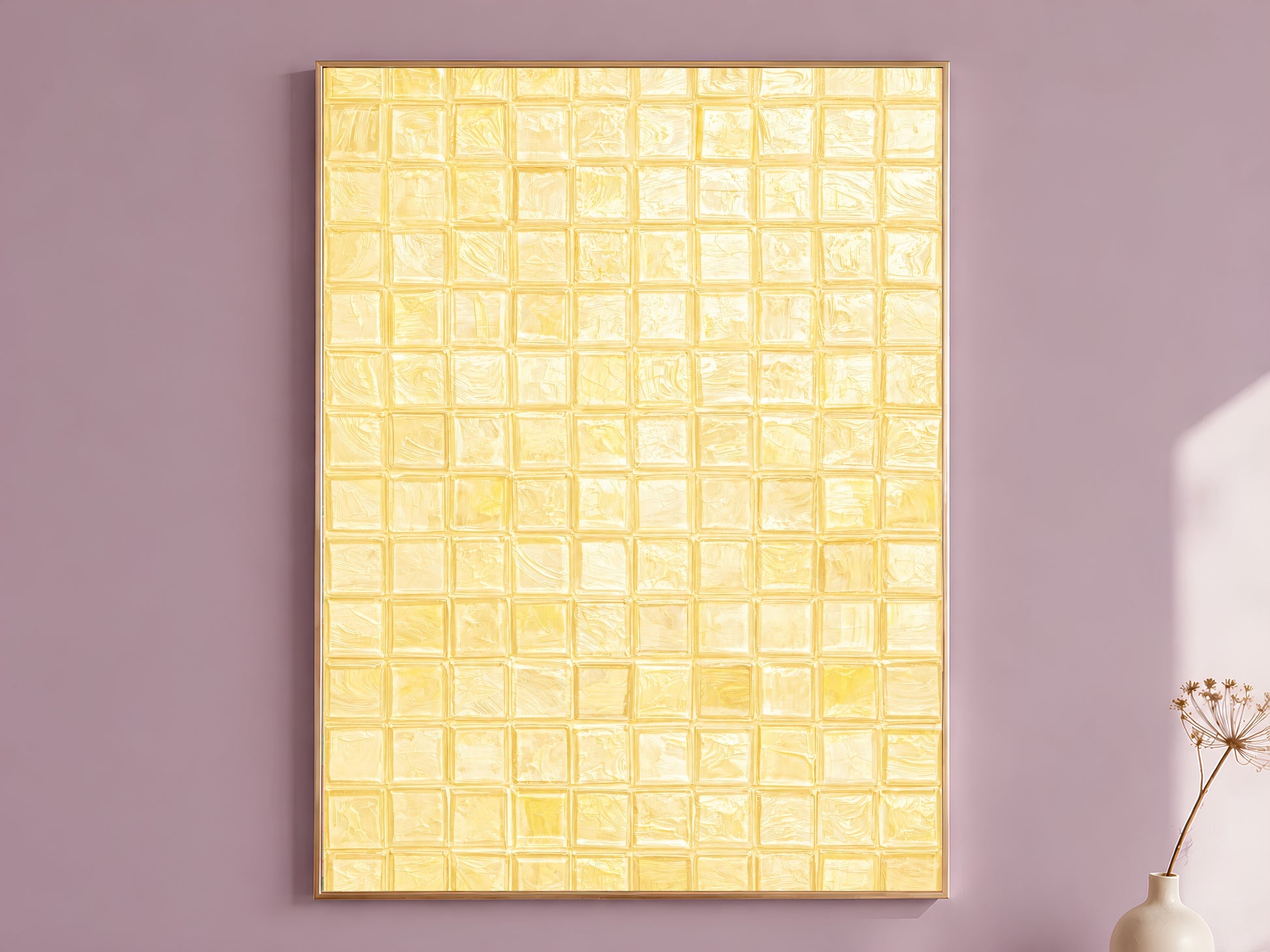 Butter yellow mosaic tile wall art print in a thin gold frame leaning against a dusty mauve wall with a dried allium stem in a cream vase beside it
