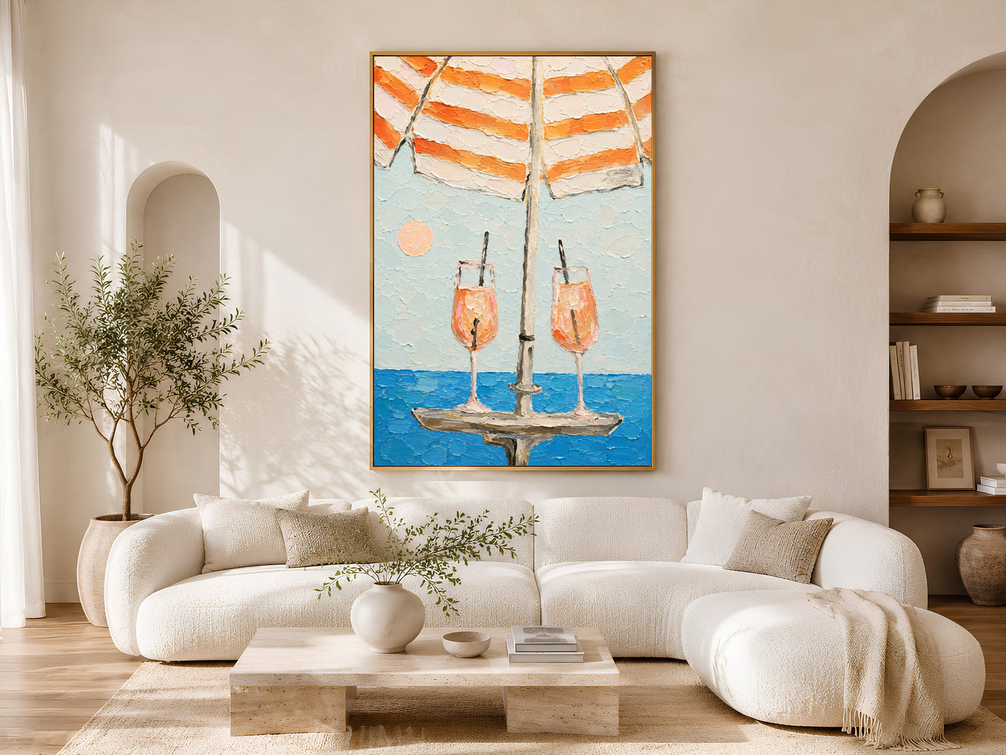 Framed aperol spritz cocktail impasto print displayed on wall in a bright Scandinavian living room with curved cream sofa, arch doorway, and olive tree
