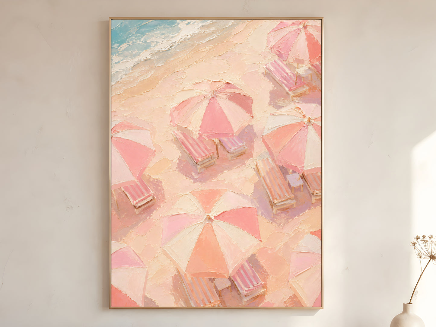 Aerial pink beach umbrella oil painting in gold frame leaning against a white wall with dried florals