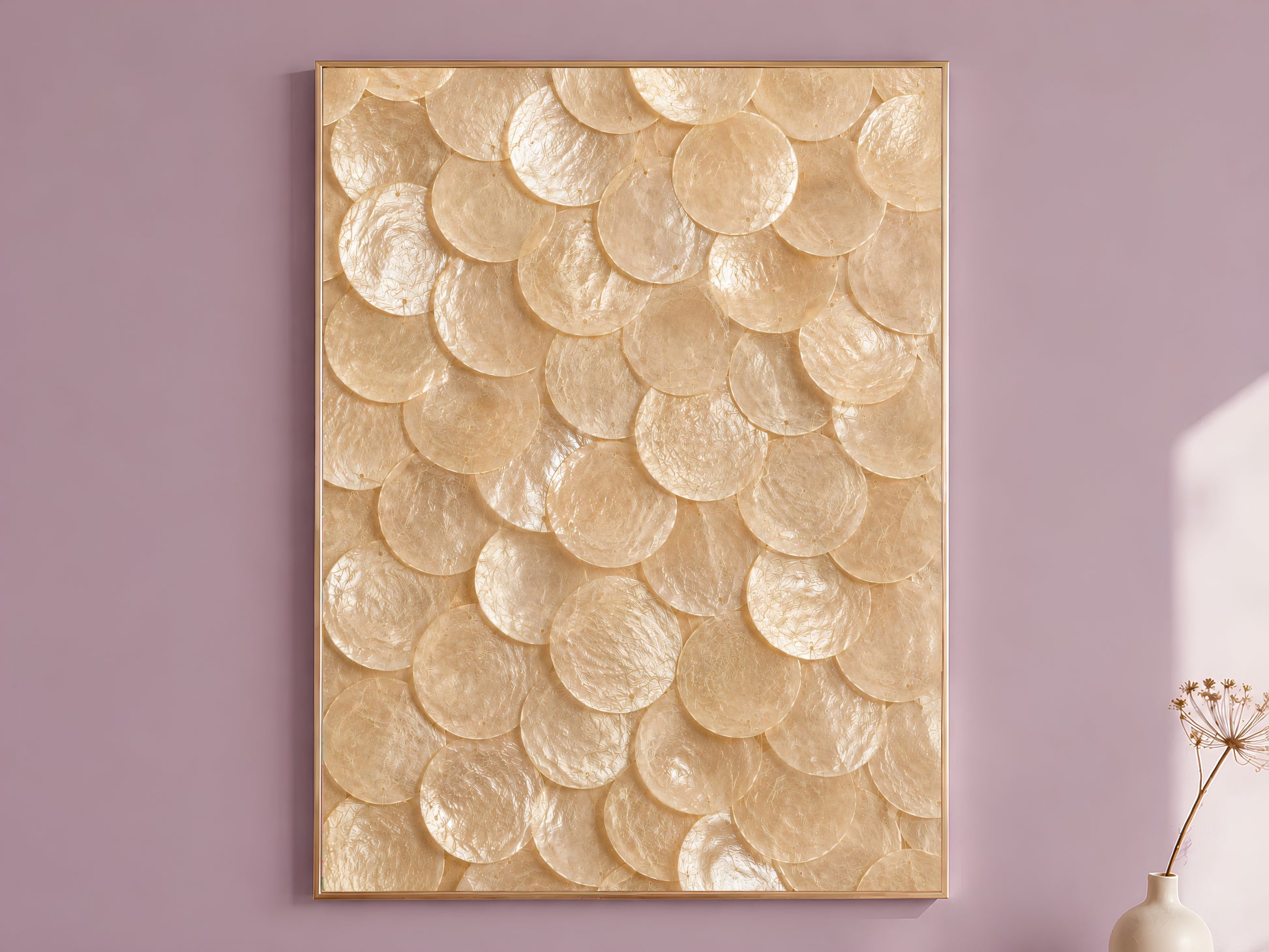 Natural capiz shell wall art in a thin gold frame, hung on a mauve wall with a vase of dried flowers.

