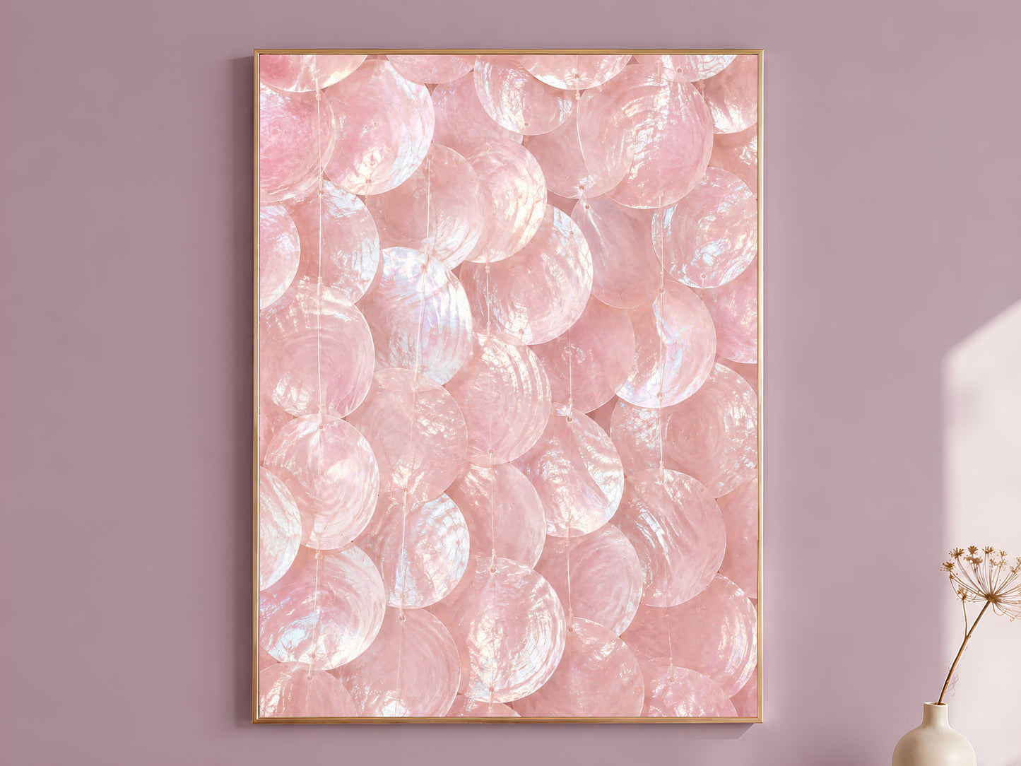 Pink capiz shell wall art print in a gold frame hanging on a dusty mauve wall beside a vase of dried flowers.
