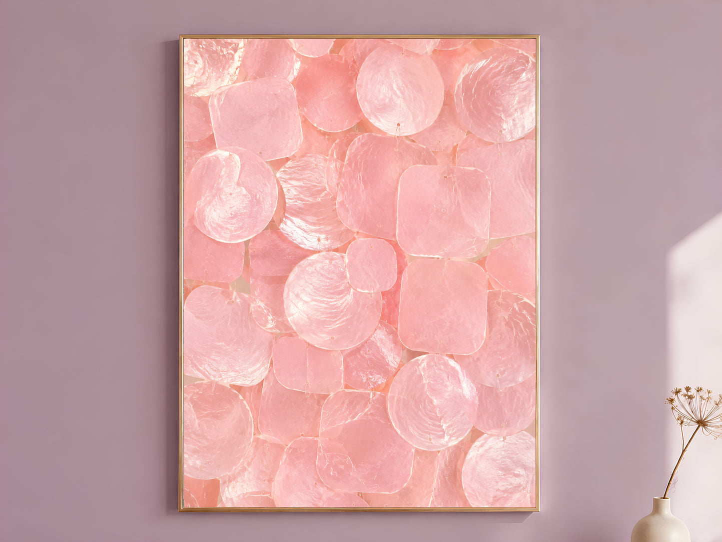Pink capiz shell wall art print in a thin gold frame, hung on a mauve wall with a vase of dried flowers.
