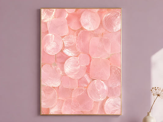 Pink capiz shell wall art print in a thin gold frame, hung on a mauve wall with a vase of dried flowers.
