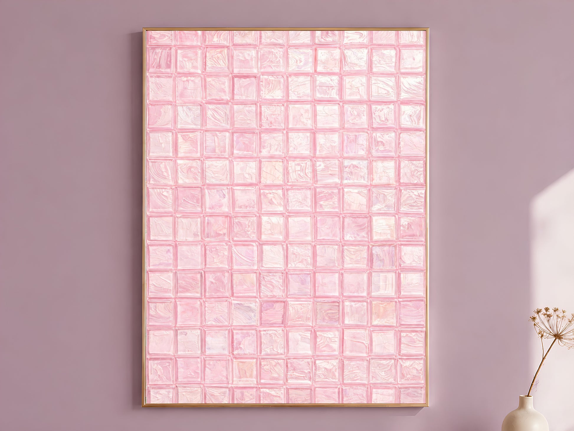 Blush pink impasto mosaic tile wall art in a thin gold frame leaning against a dusty mauve wall with a dried allium stem in a cream vase beside it
