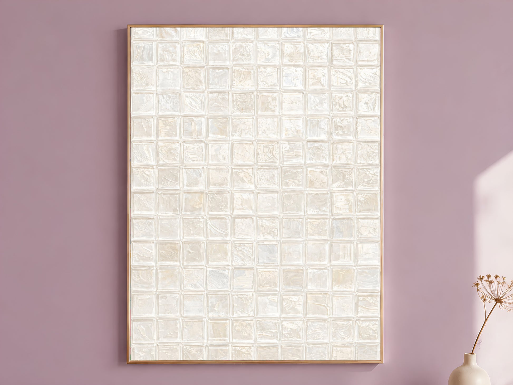 White pearl impasto mosaic tile wall art in a thin gold frame leaning against a dusty mauve wall with a dried allium stem in a cream vase beside it
