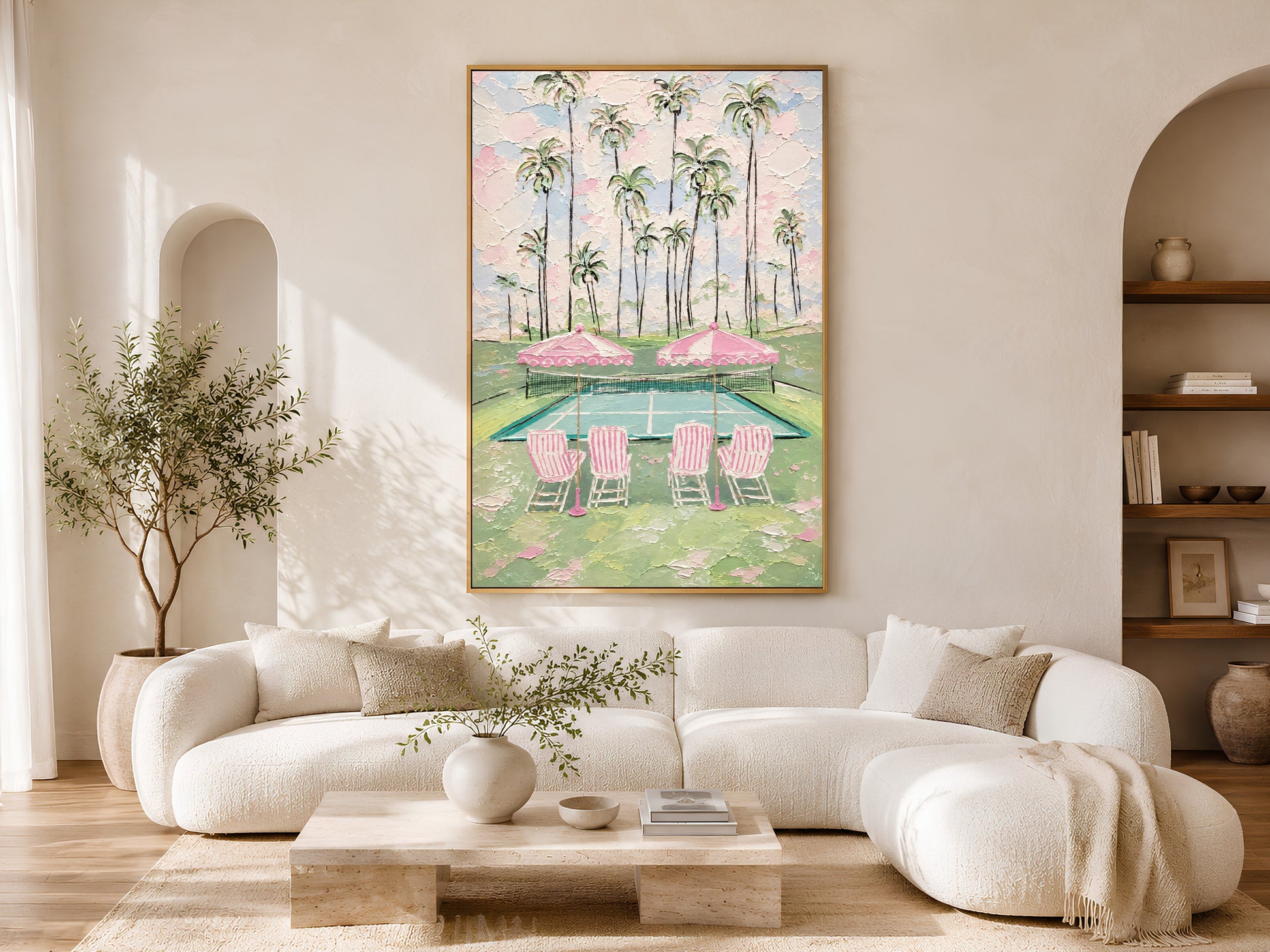Gold-framed preppy pink tennis court wall art above a low cream coffee table in a bright minimalist living room with a curved sofa and warm natural light
