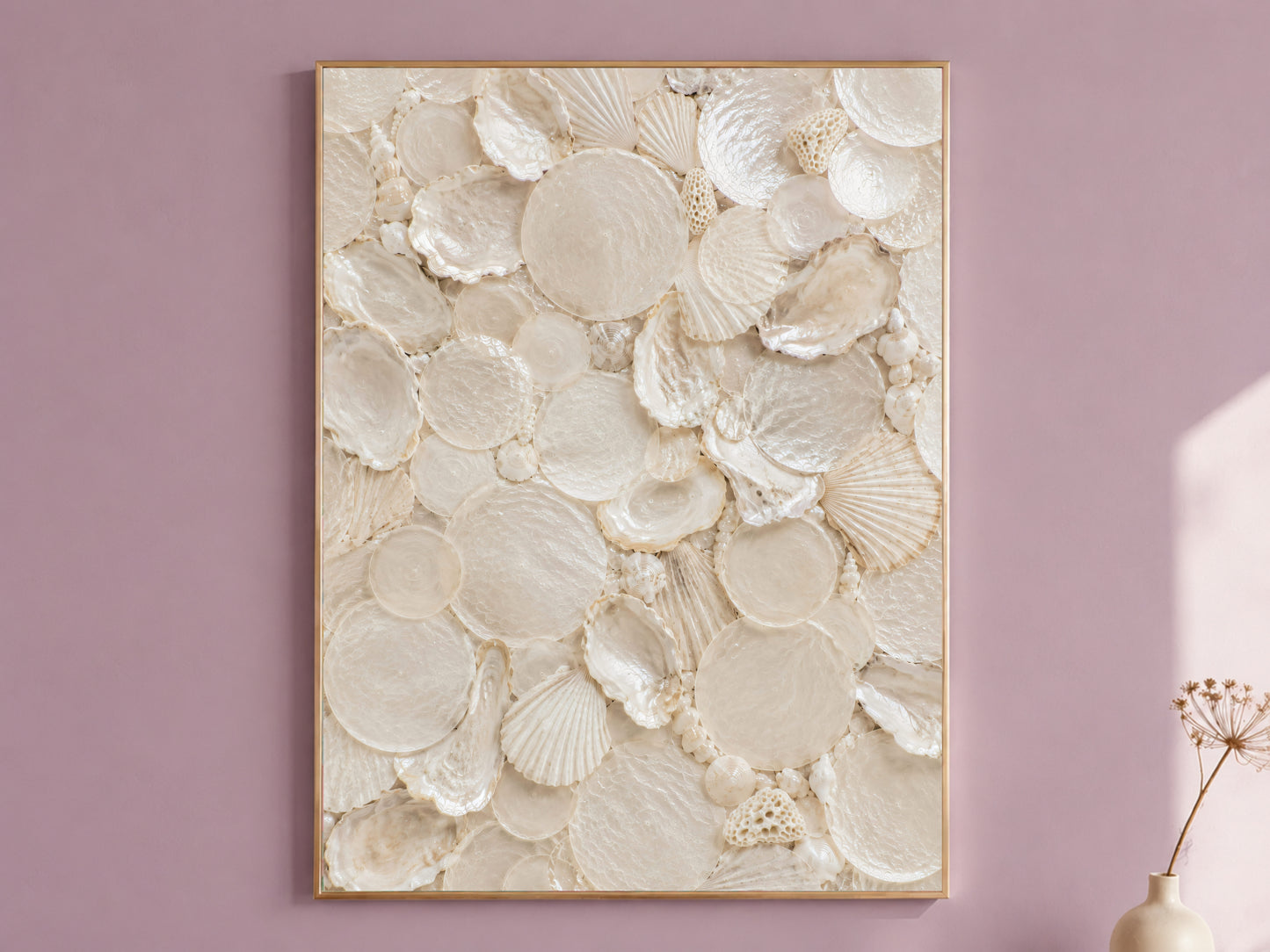 Shell collector wall art in a thin gold frame hanging on a dusty mauve wall, styled with a small dried flower vase.