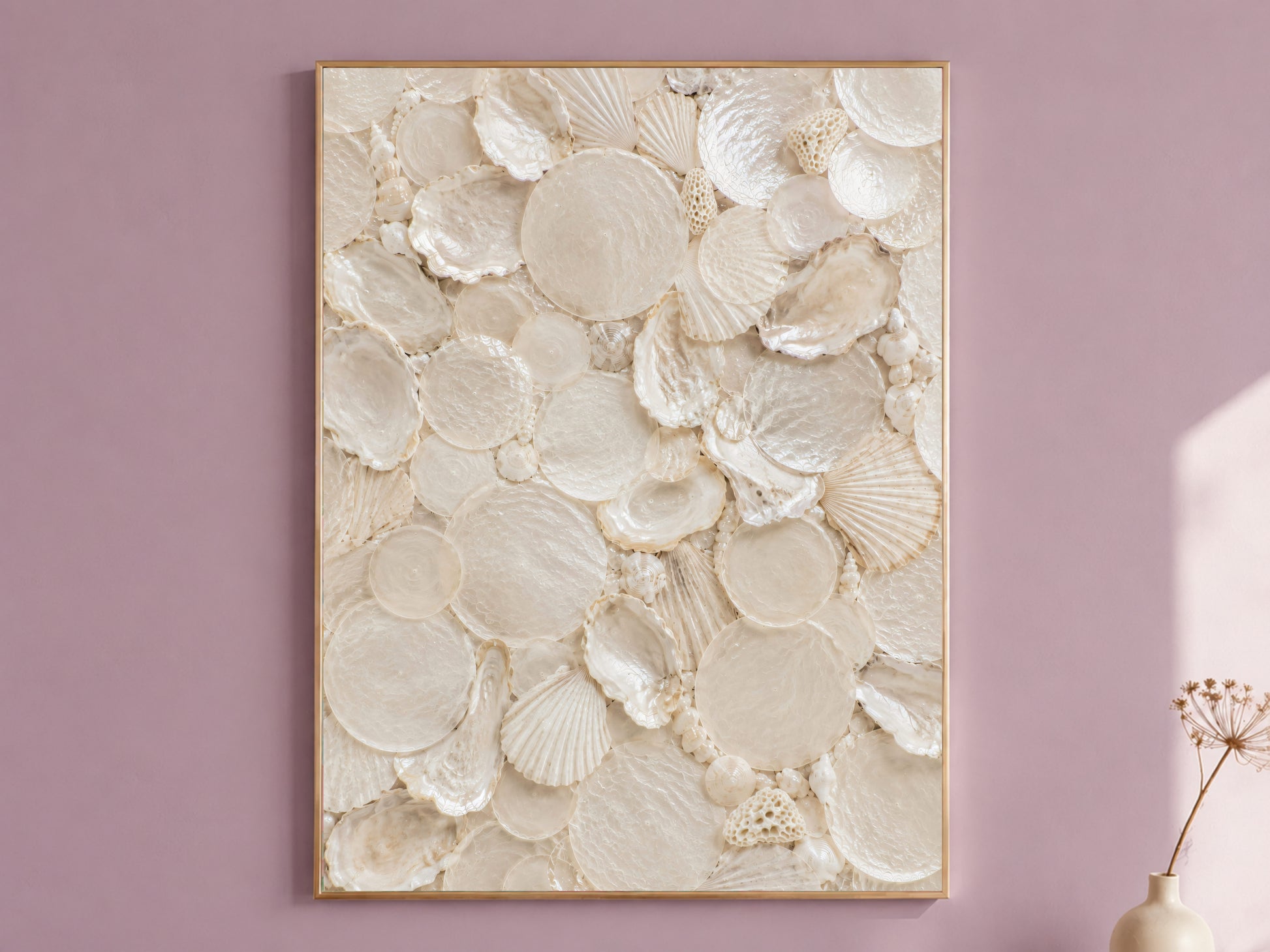 Shell collector wall art in a thin gold frame hanging on a dusty mauve wall, styled with a small dried flower vase.