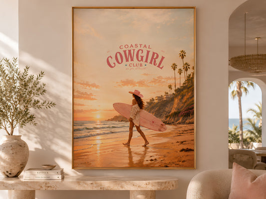 Coastal Cowgirl Club surfer girl sunset print in a gold frame displayed on a wooden console table in a warm neutral living room with olive tree and arched doorway

