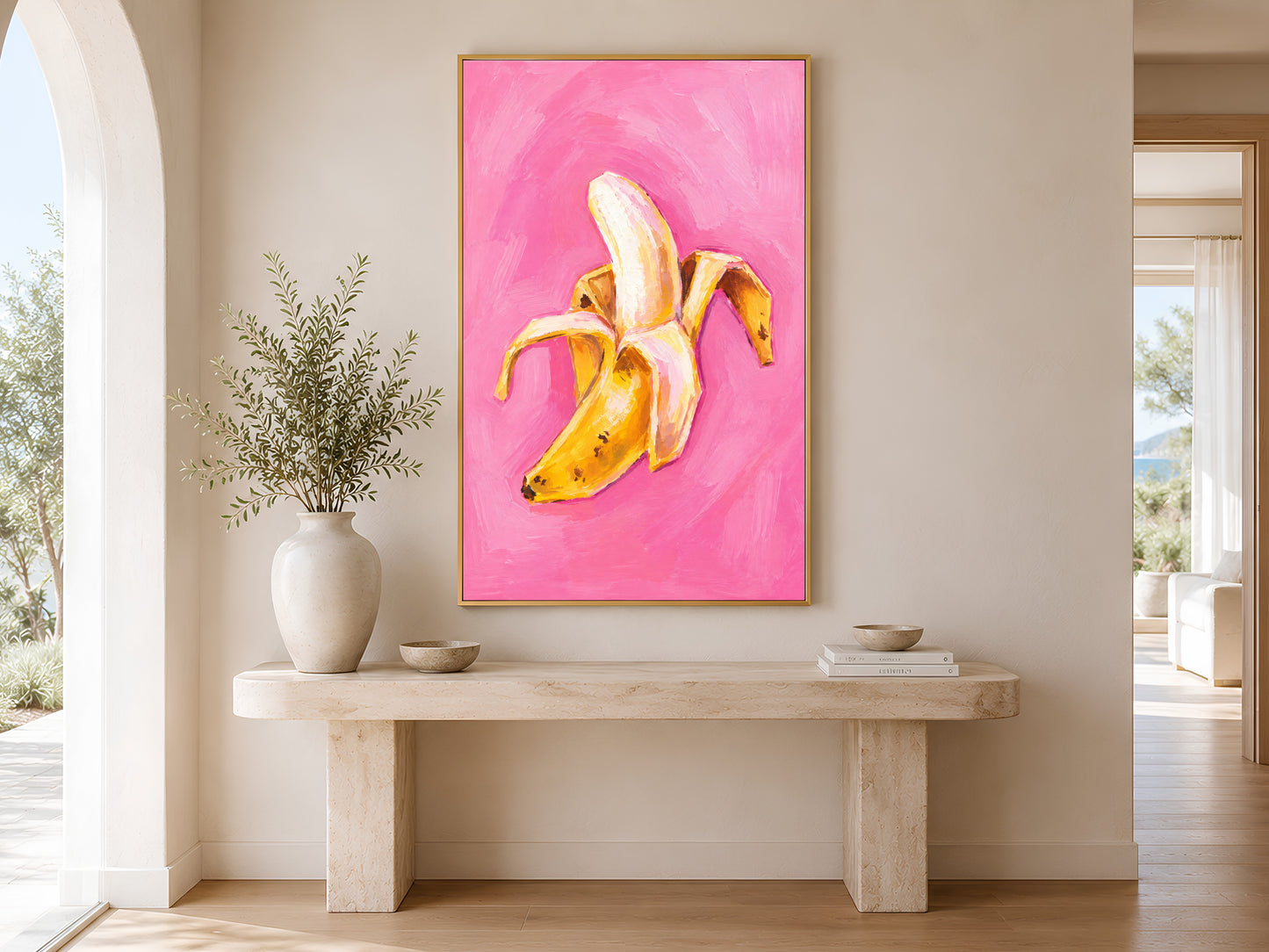 Framed impasto peeled banana print on warm white wall in minimal entryway with wooden console table and tall vase
