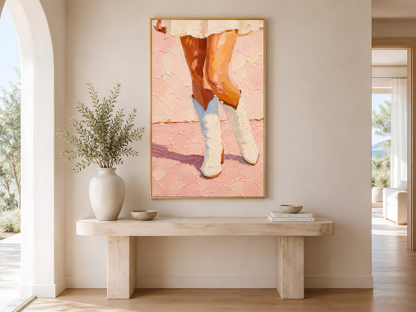 Framed cowgirl boots wall art displayed on wall above a wooden console table with large white ceramic vase in a minimal neutral entryway
