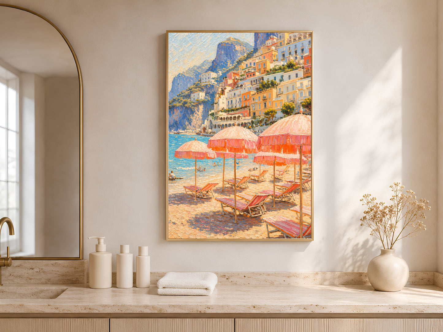 Bathroom vanity styled with folded towels and glass bottles beside a sunlit window, framed Positano beach umbrellas print hanging above the counter.
