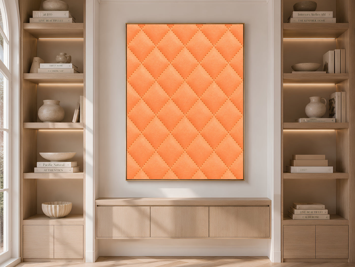 Quilted leather wall art in coral orange framed above a console table between built-in bookshelves
