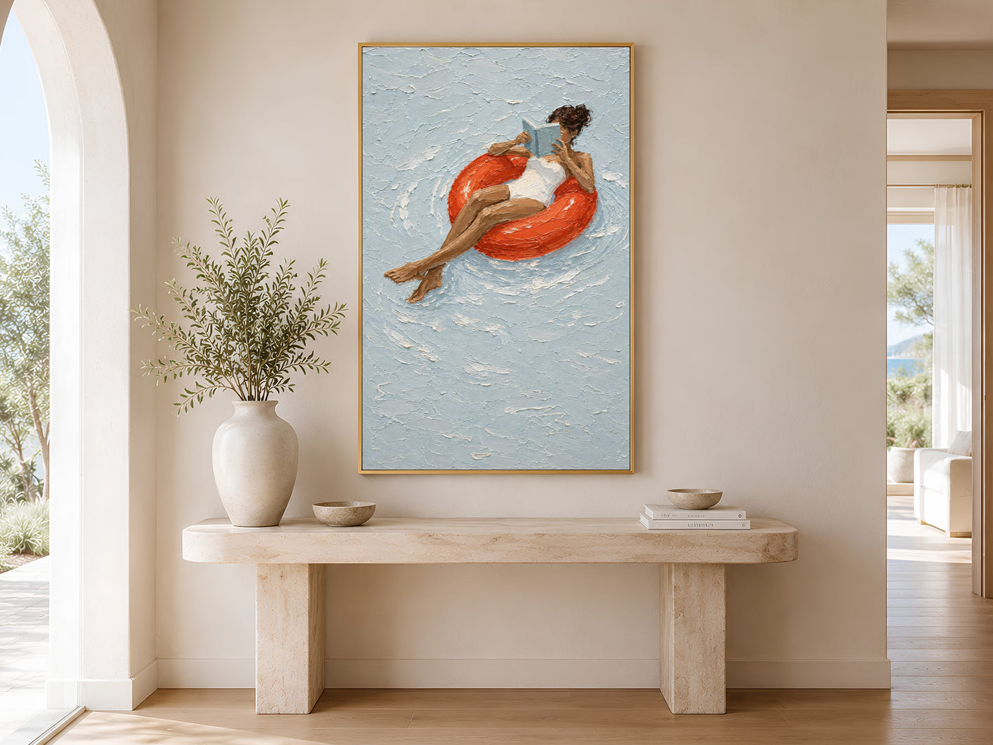 Gold-framed woman on red pool float print above a minimalist console table with a tall round white vase in a neutral entryway with warm natural light
