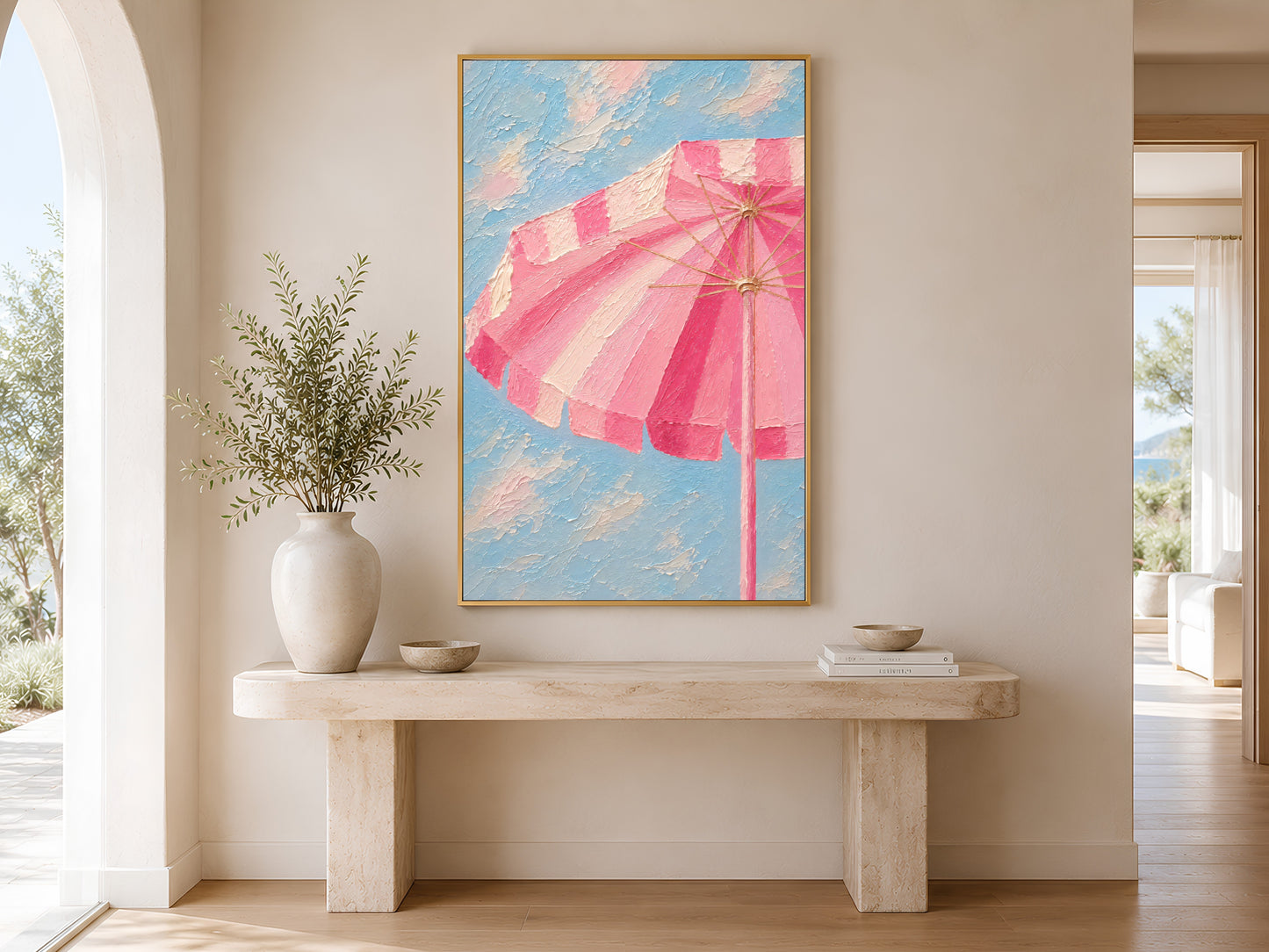 Framed pink striped beach umbrella painting print in a bright coastal living room with white sofa, wooden coffee table, palm tree and ocean view
