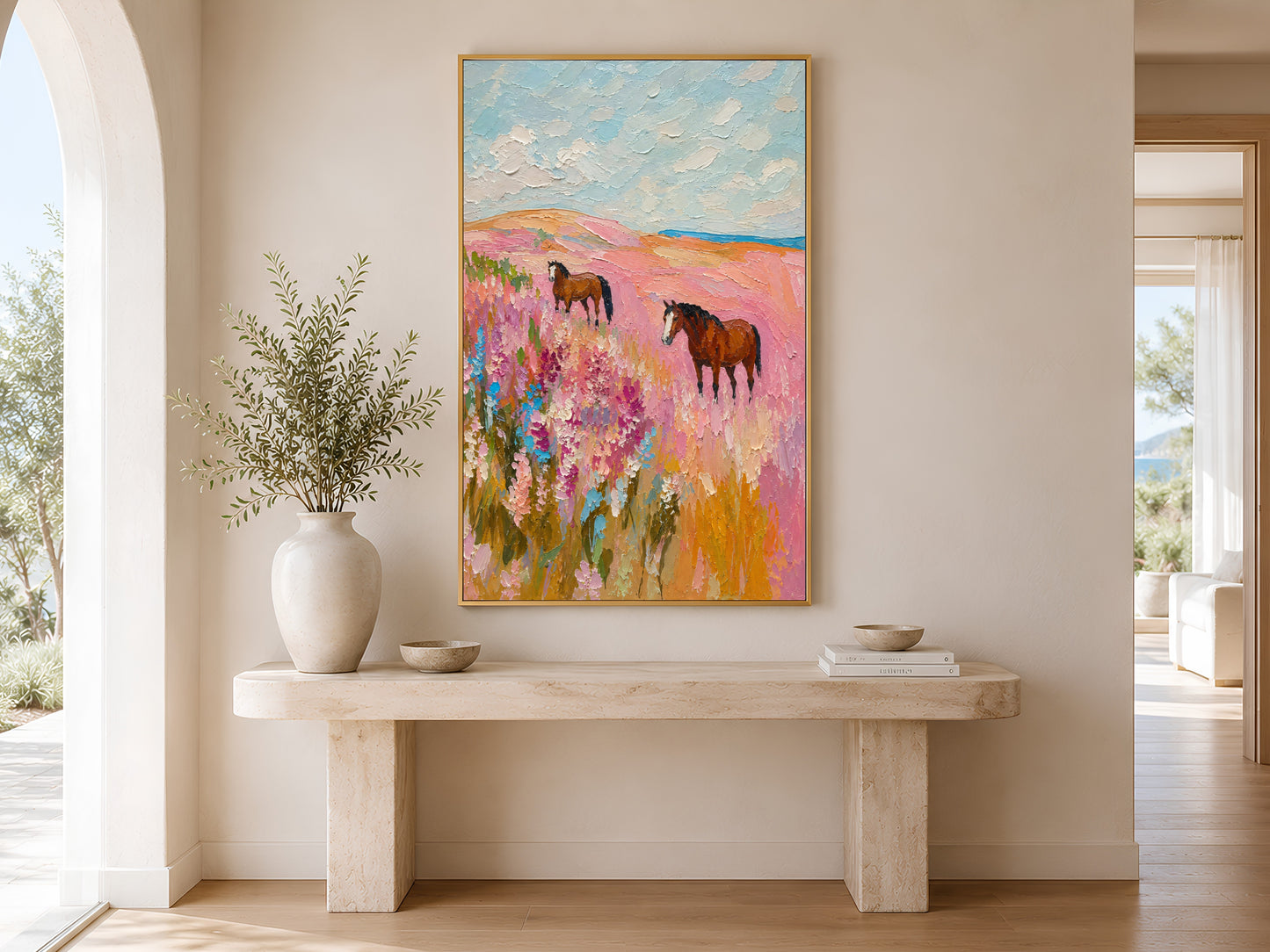 Pink wildflower horse impasto print in a gold frame above a minimalist console table with round white vases in a warm neutral entryway
