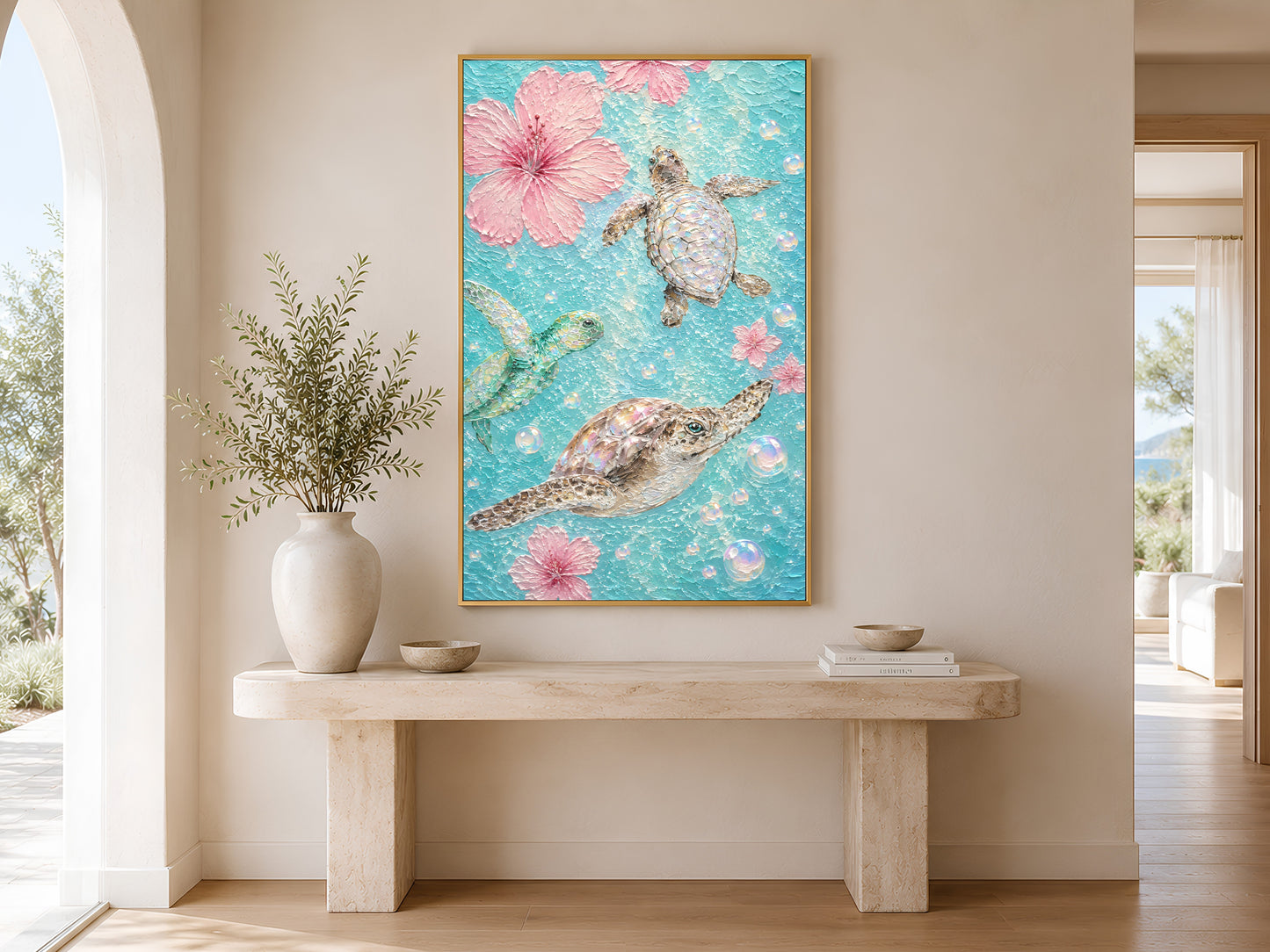 Gold-framed pink hibiscus and sea turtle wall art above a minimalist stone console table with a round white vase in a bright neutral entryway with arched wall detail
